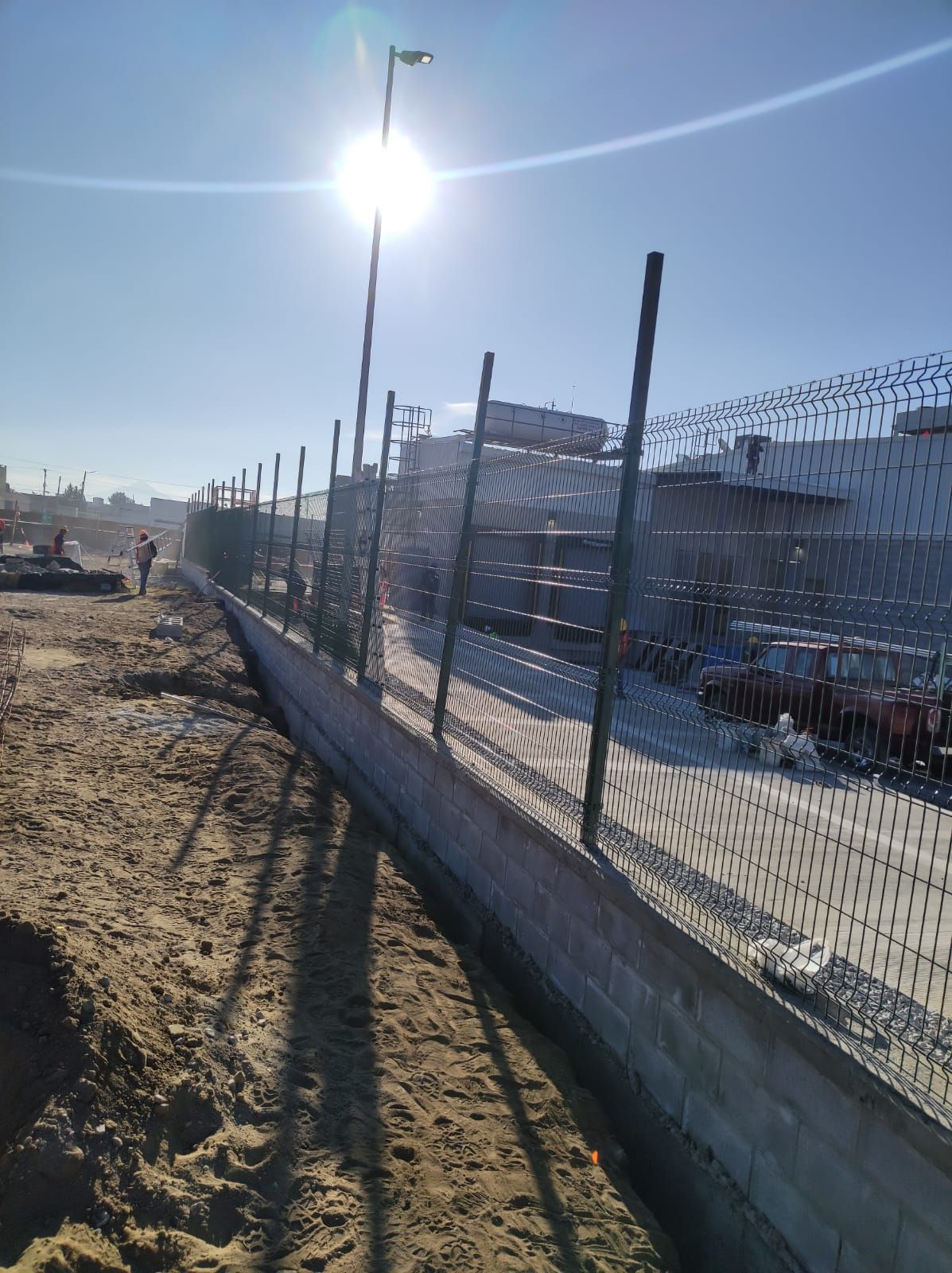 Una valla con alambre de púas delante de un edificio en construcción en un día soleado.