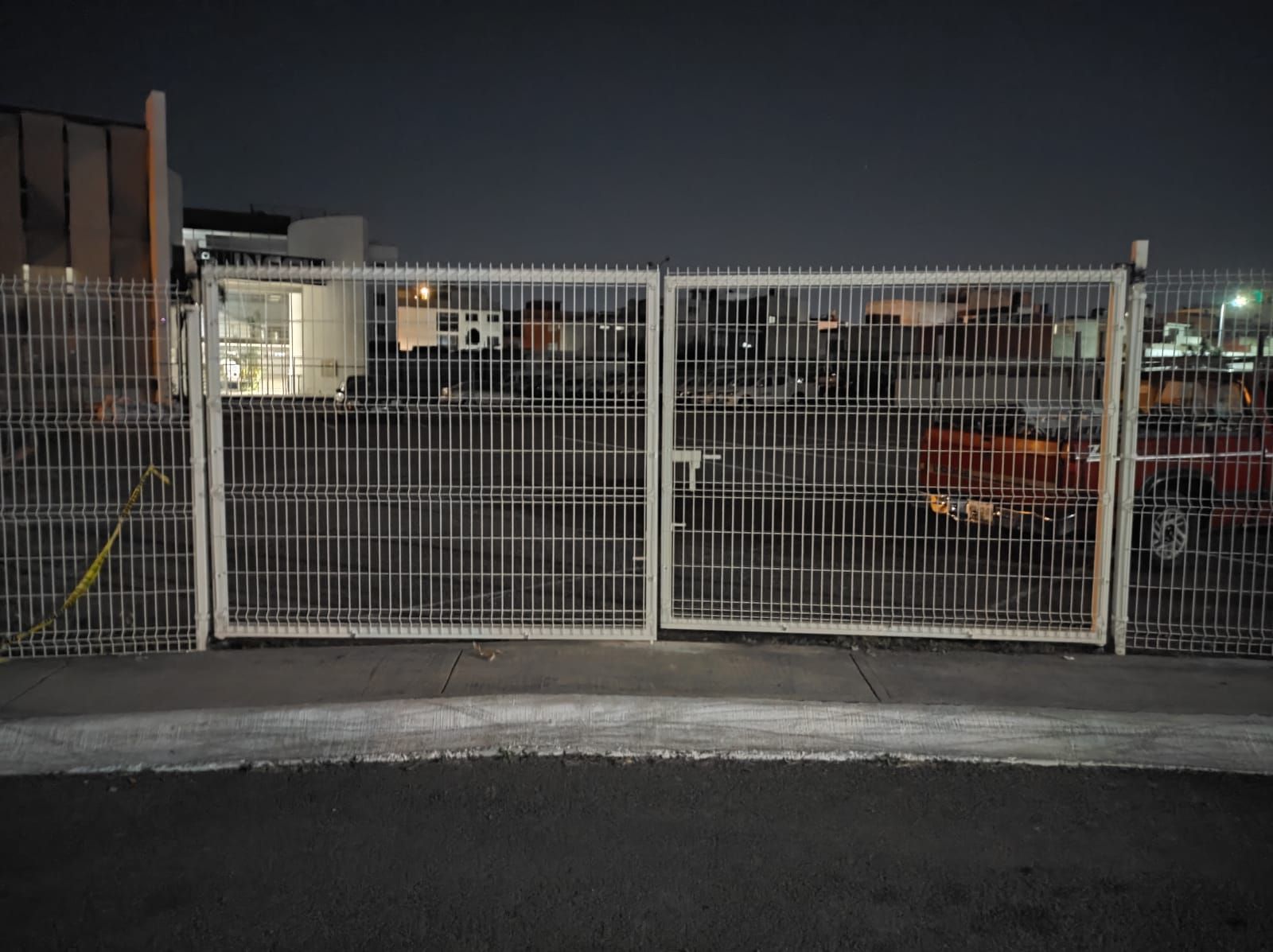 Puertas de metal blanco cerradas, bloqueando la vista de los edificios y vehículos estacionados por la noche.