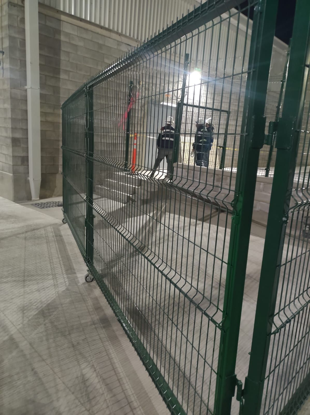 Valla metálica verde con tres figuras dentro de un área en construcción.