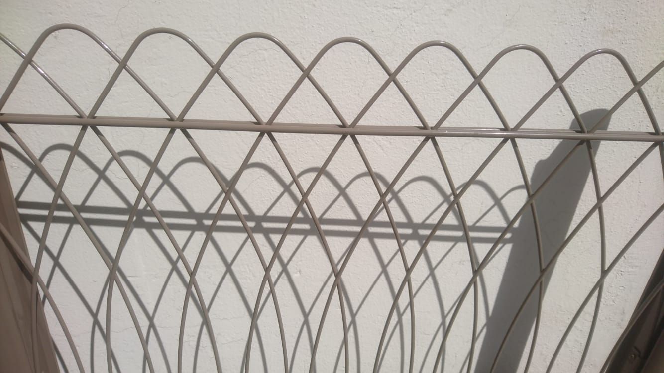 Sombra de una valla metálica decorativa sobre una pared blanca, creando un patrón de diamantes.