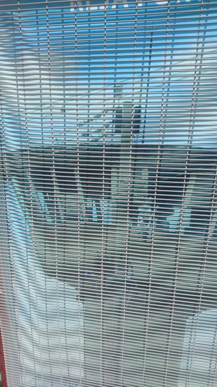 Valla de malla metálica con fondo borroso de cielo y estructuras.