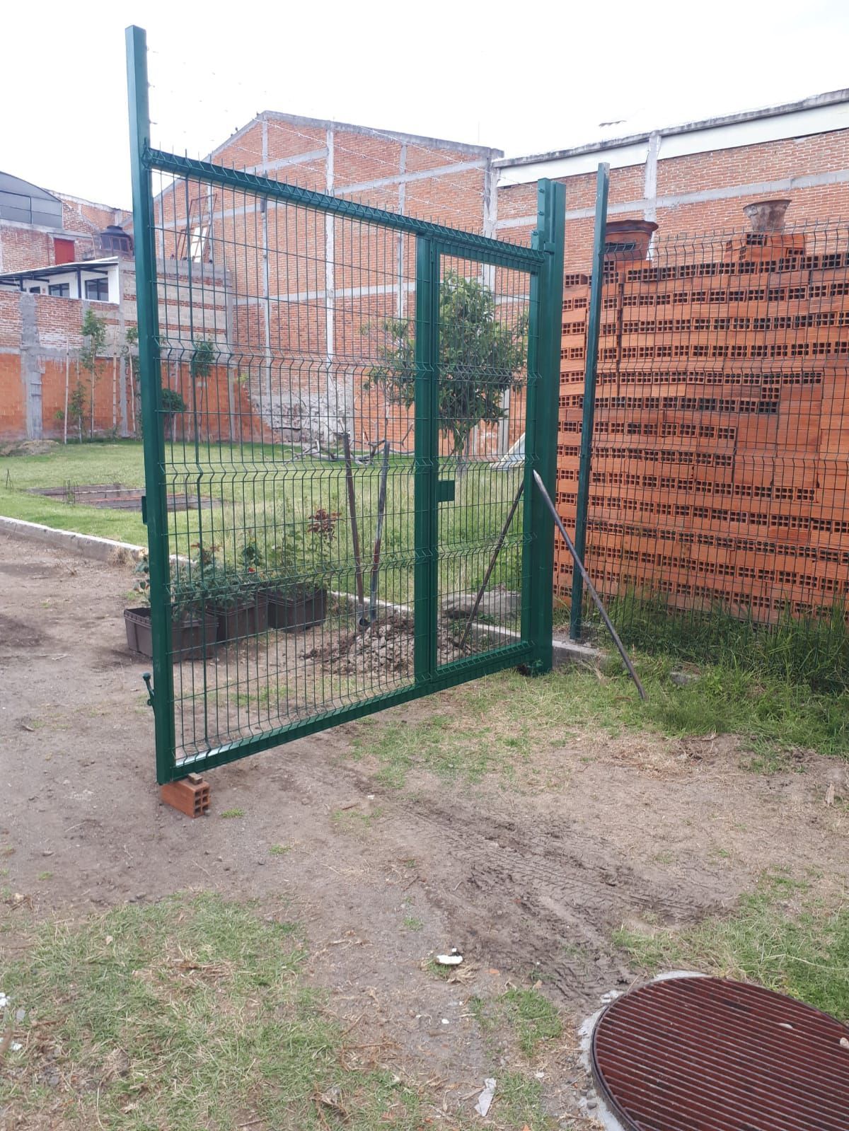 Portón metálico verde, abierto, que da a un patio con paredes de ladrillo, día nublado.