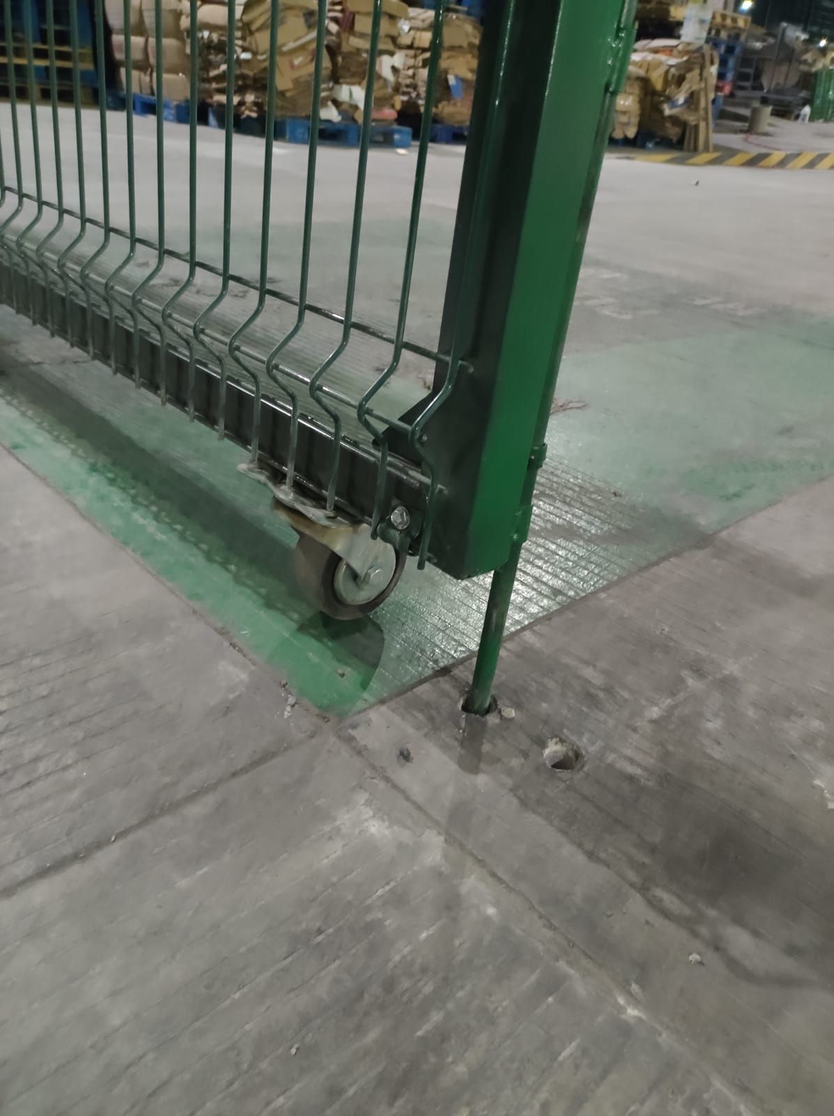 Puerta metálica verde con ruedas sobre suelo de hormigón.