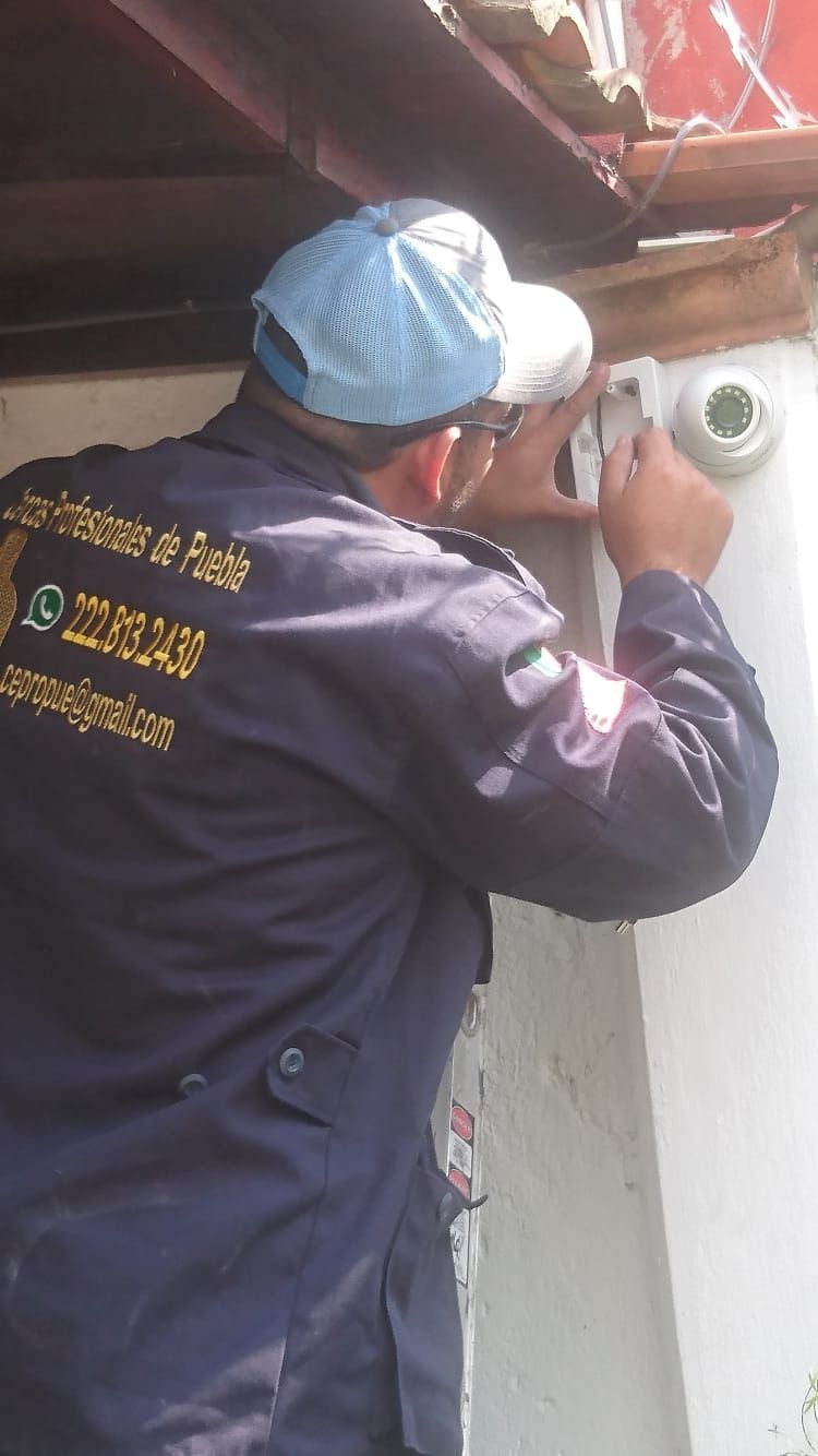 Persona con uniforme de la marina instalando una cámara de seguridad en el exterior de un edificio.