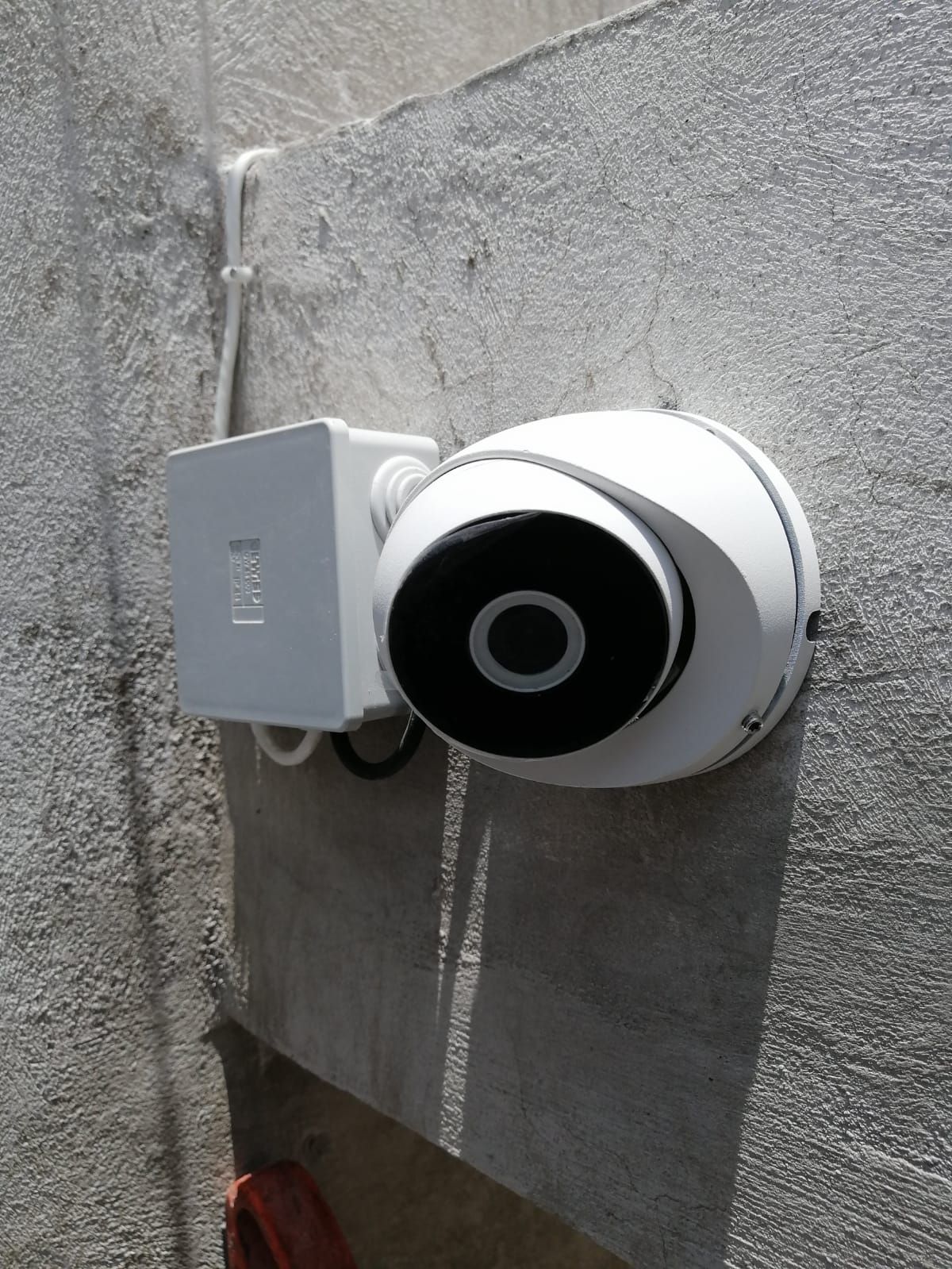 Cámara de seguridad blanca y caja de conexiones montadas en una pared de estuco gris rugoso.
