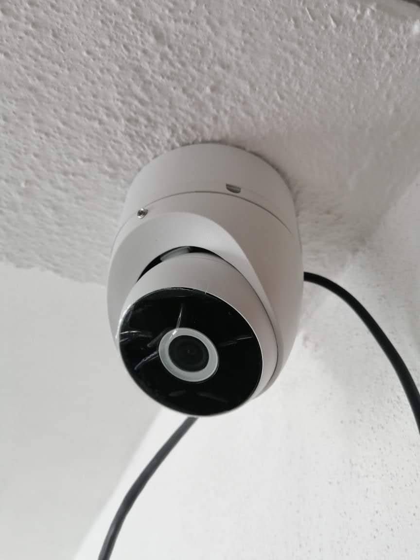 Cámara de seguridad blanca montada en un techo blanco, cable negro conectado.