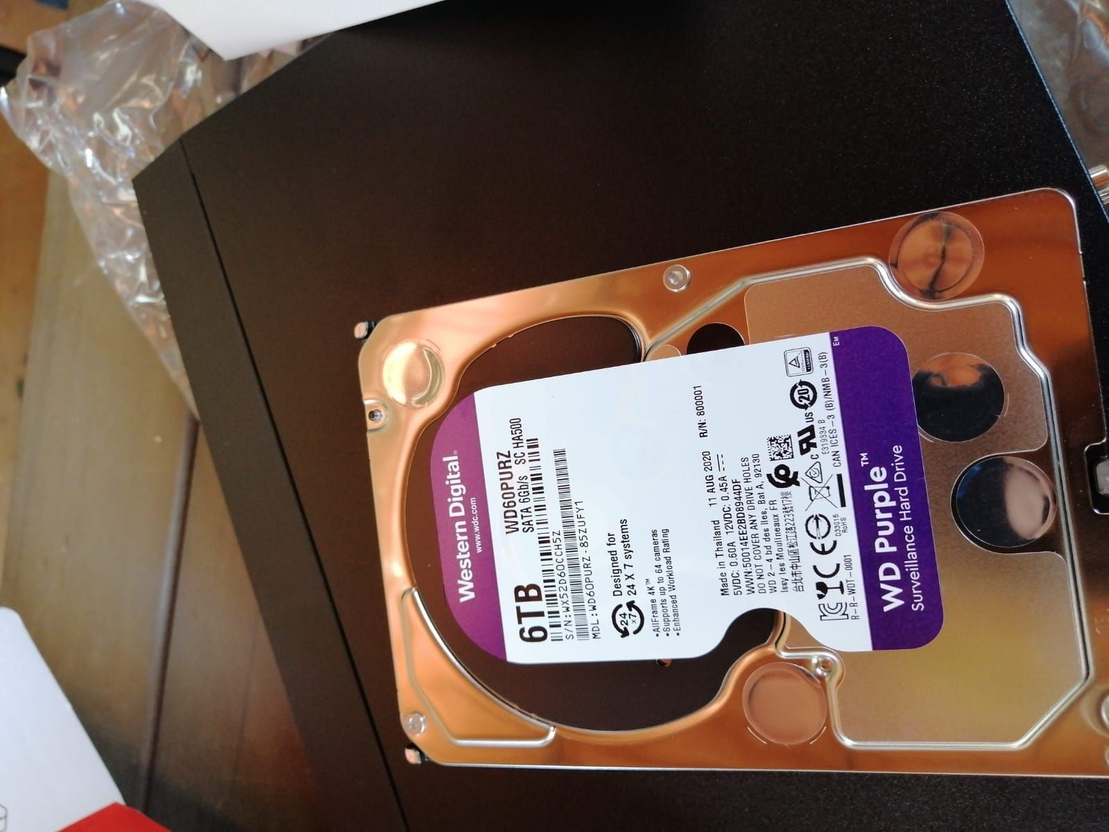 Un disco duro Western Digital WD Purple de 6 TB, con etiqueta violeta, junto a una carcasa de ordenador de color negro.