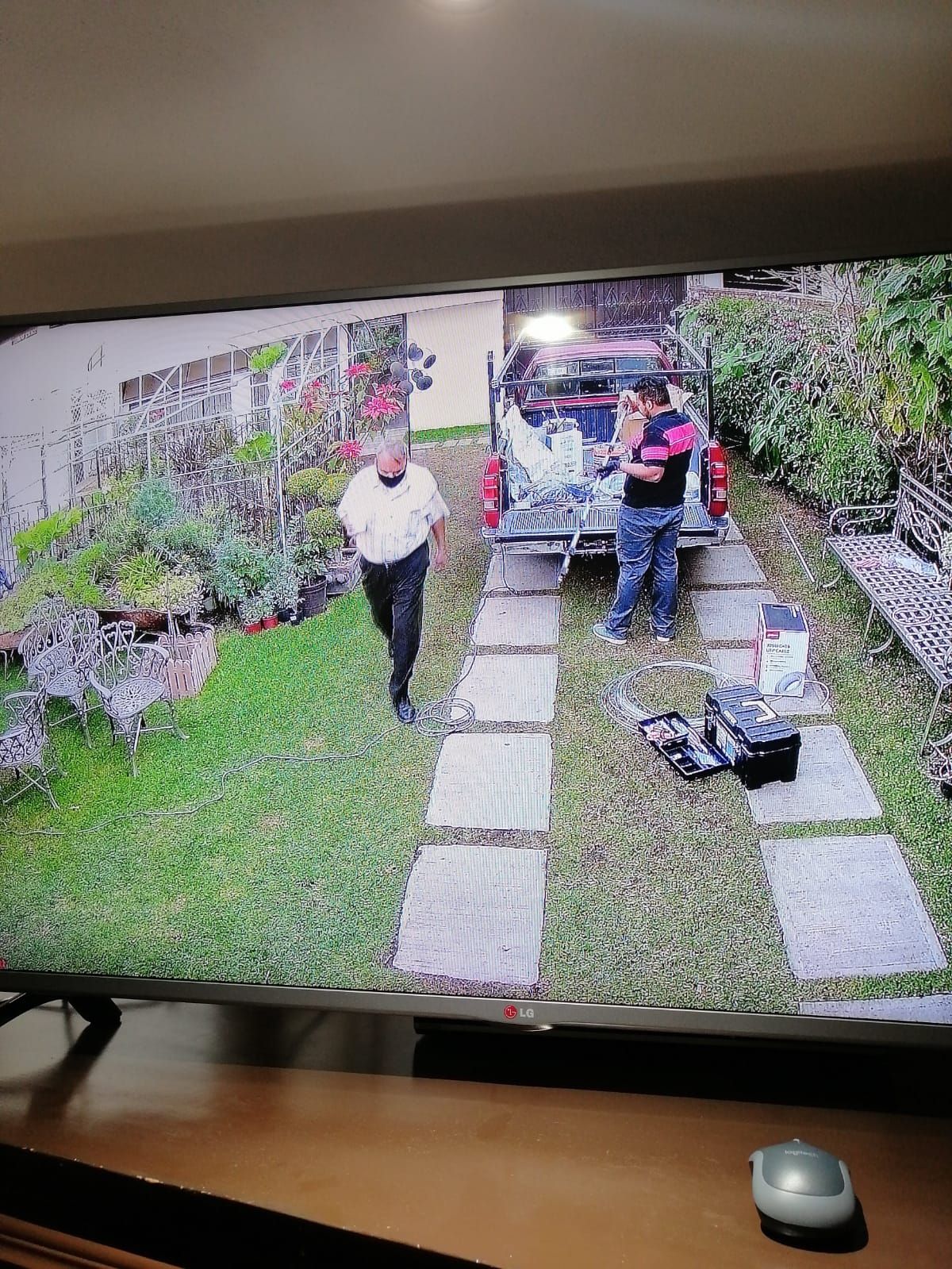 Dos hombres cerca de un camión en una entrada. Uno camina, el otro trabaja en el camión. Césped verde y camino de piedra.