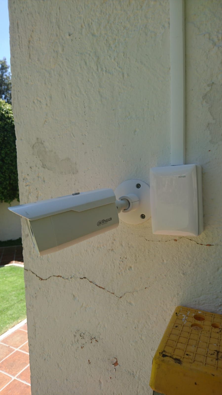 Cámara de seguridad blanca montada en una pared beige texturizada, con conducto y caja eléctrica.