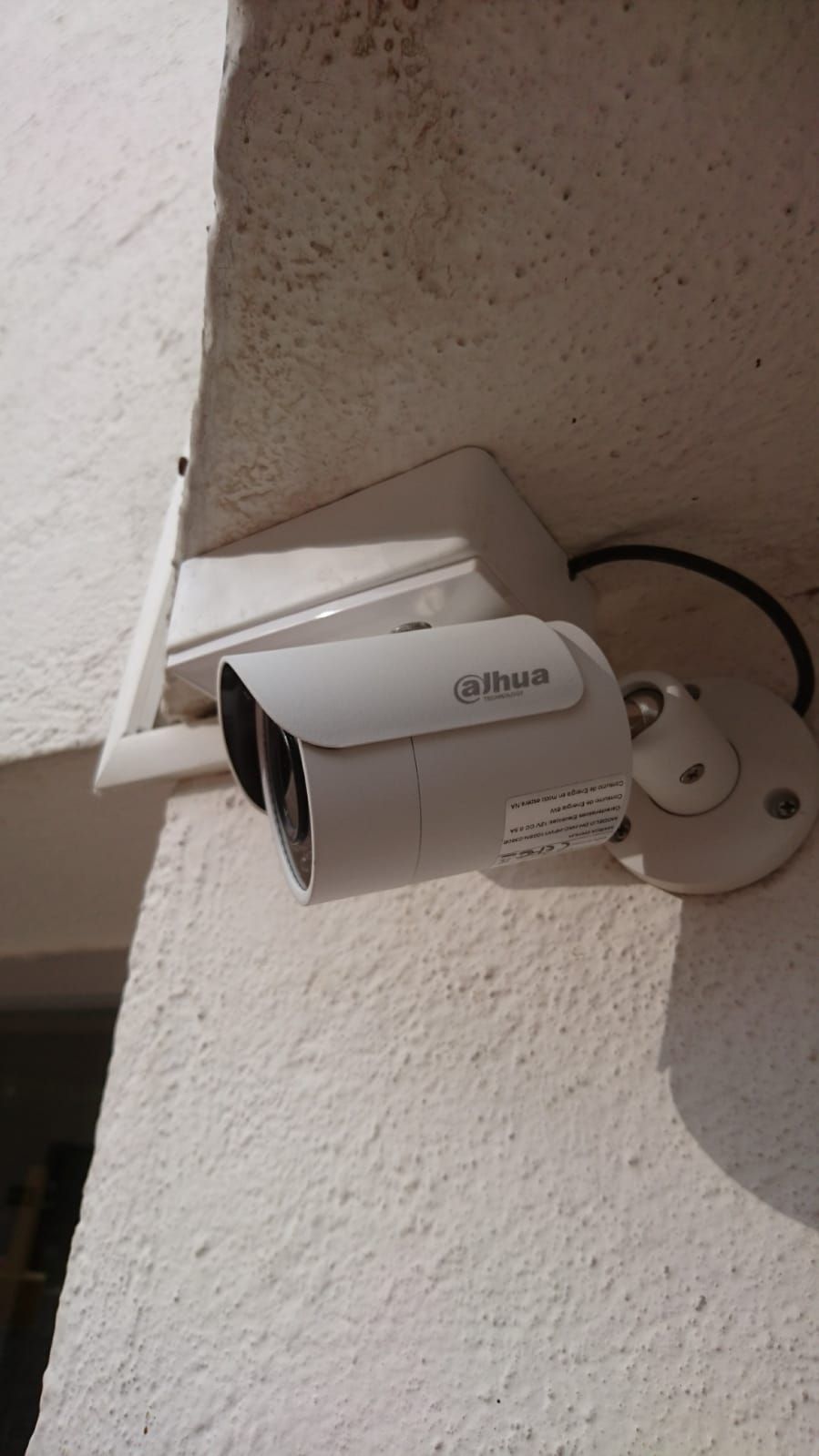 Cámara de seguridad Dahua blanca montada en una pared blanca texturizada.