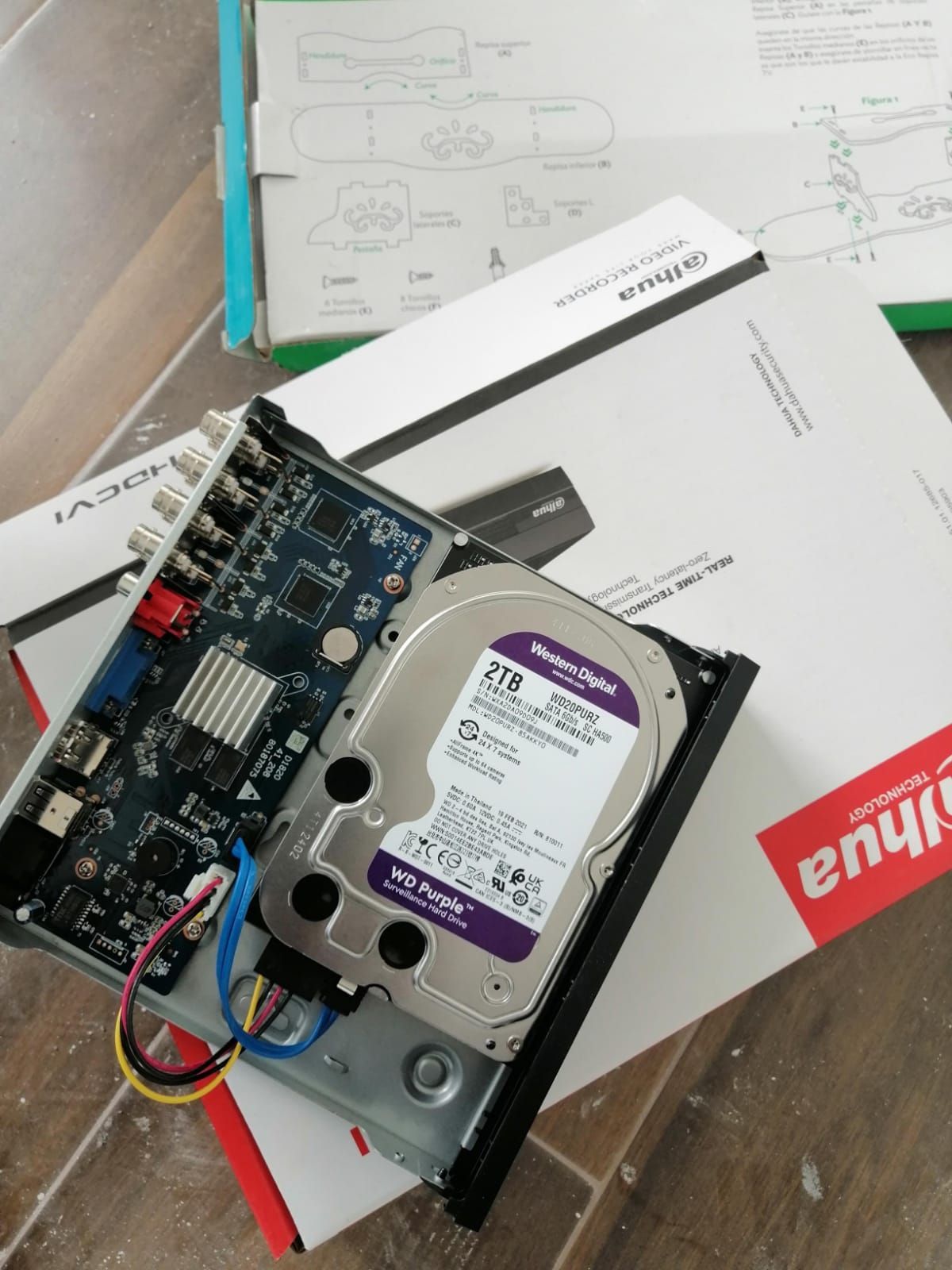 Un DVR Dahua con una carcasa abierta que revela un disco duro, una placa de circuito y manuales de instrucciones en el piso.