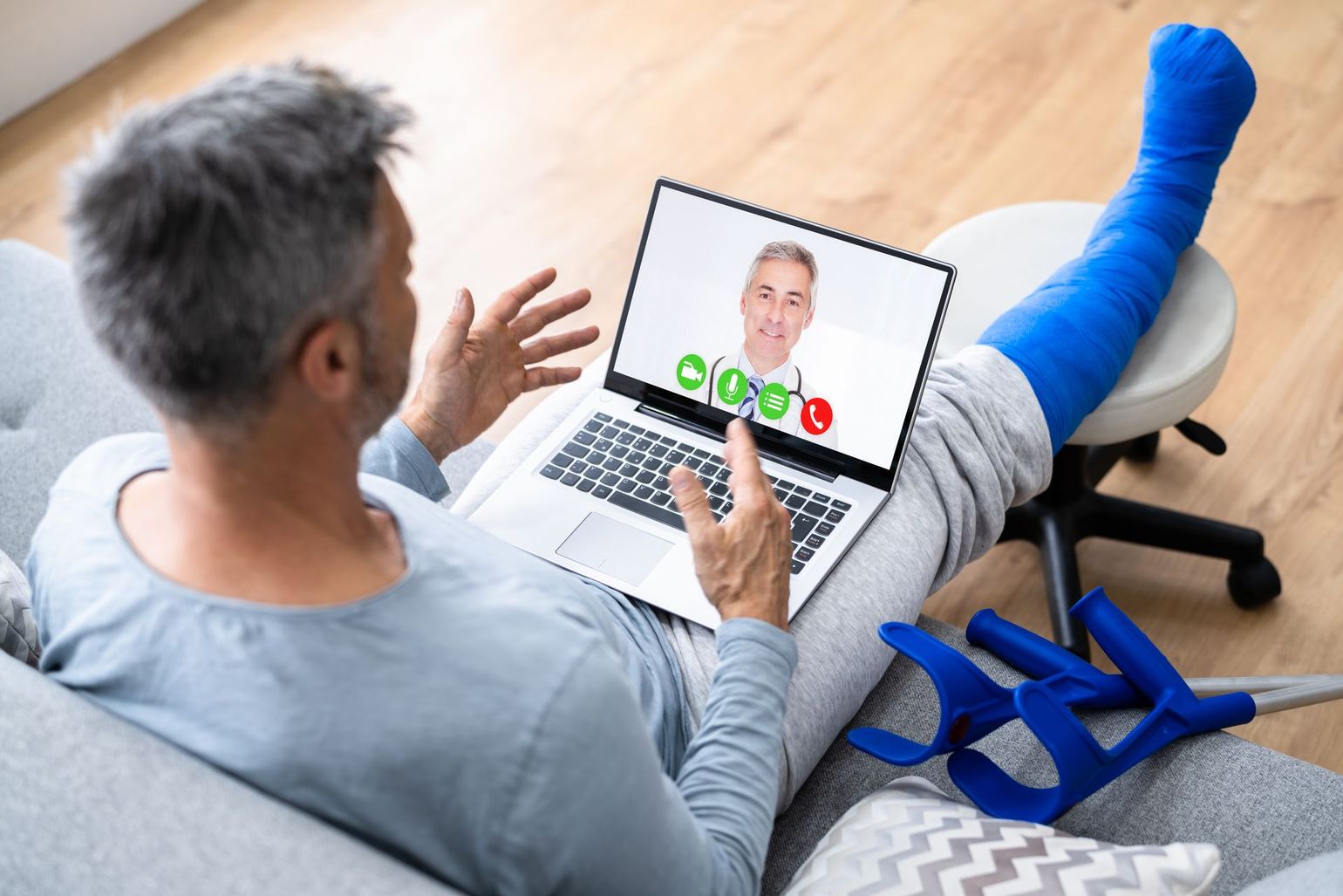 A man with a cast on his leg is sitting on a couch using a laptop computer.