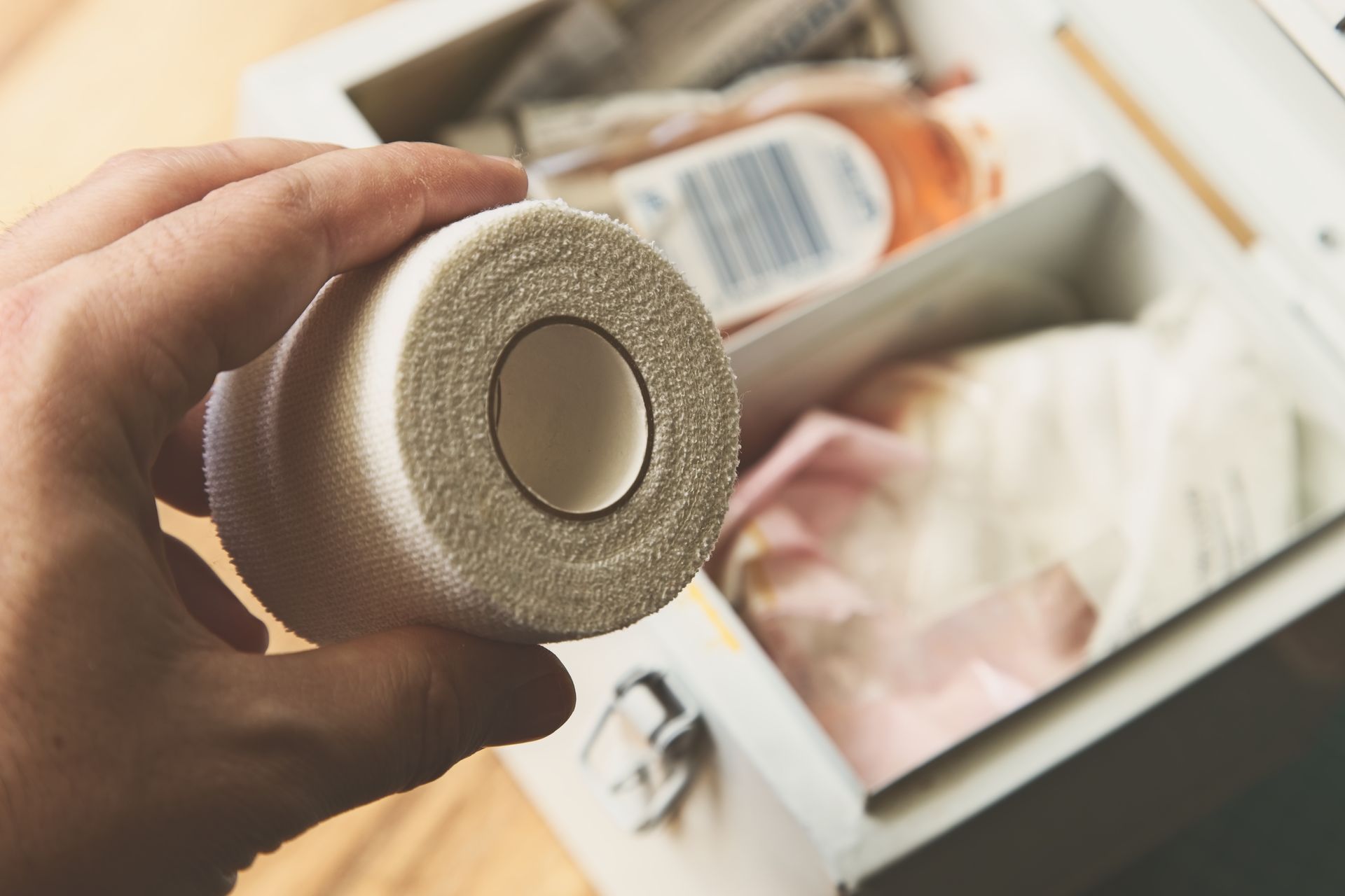 A person is holding a roll of bandage in front of a first aid kit.