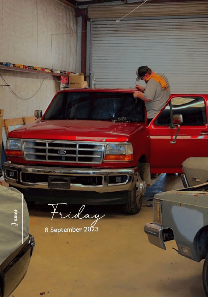 A man is standing next to a red truck in a garage.