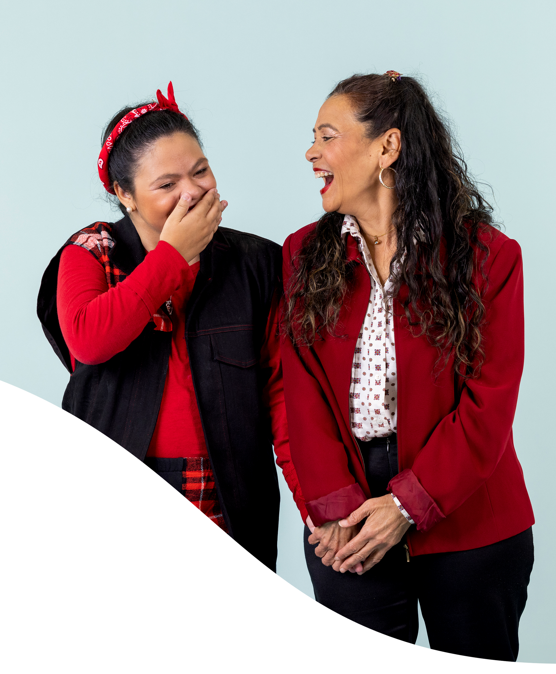 Two women are standing next to each other and one is covering her mouth with her hand.