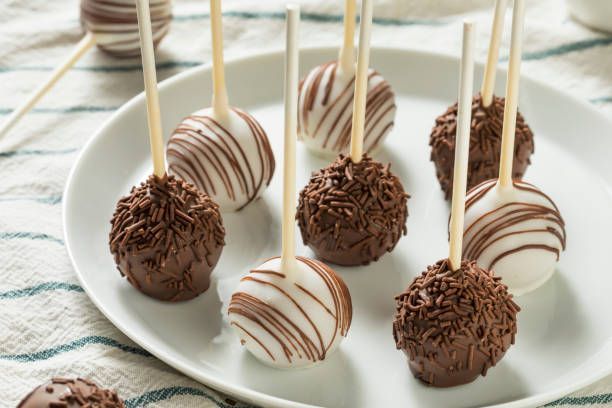 Chocolate cake pops, some with sprinkles, others with white chocolate drizzle, on a white plate.