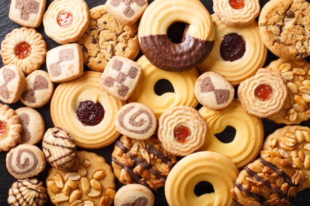Assorted cookies, including shortbread, chocolate-dipped, and peanut butter, arranged on a dark surface.
