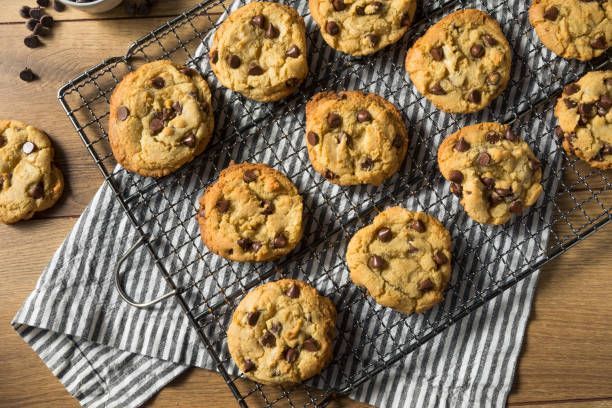 Chocolate chip cookies on a wire rack over a striped cloth on a wooden table.