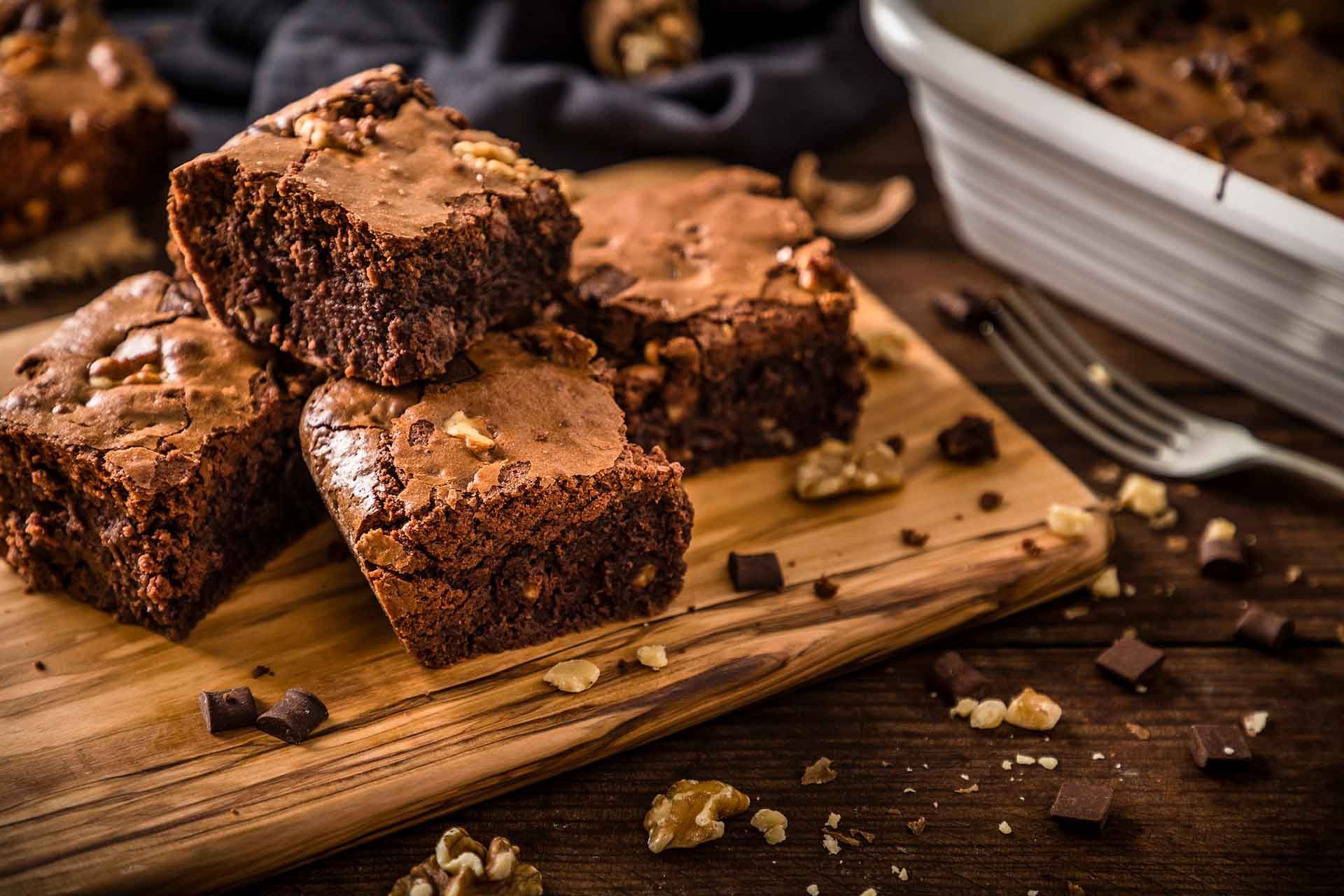 Brownies on wooden cutting board with walnuts and chocolate pieces.
