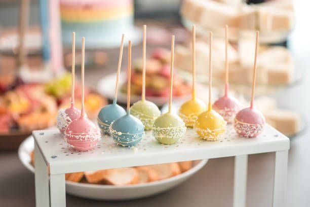 Cake pops in pastel colors on a white stand at a party.