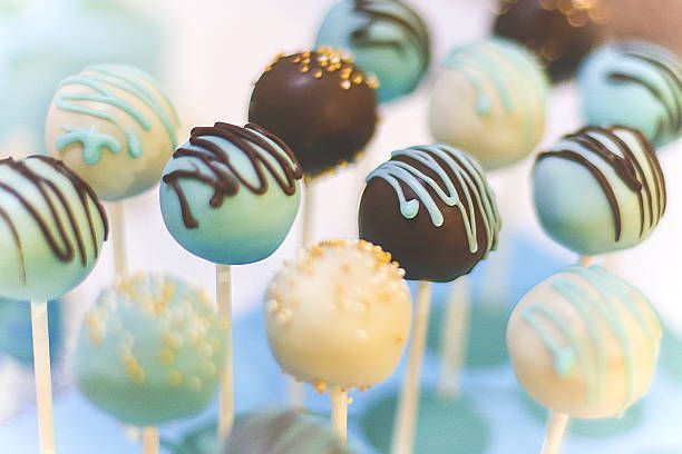 Cake pops on sticks, various colors: blue, brown, and white, with drizzled chocolate and sprinkles.