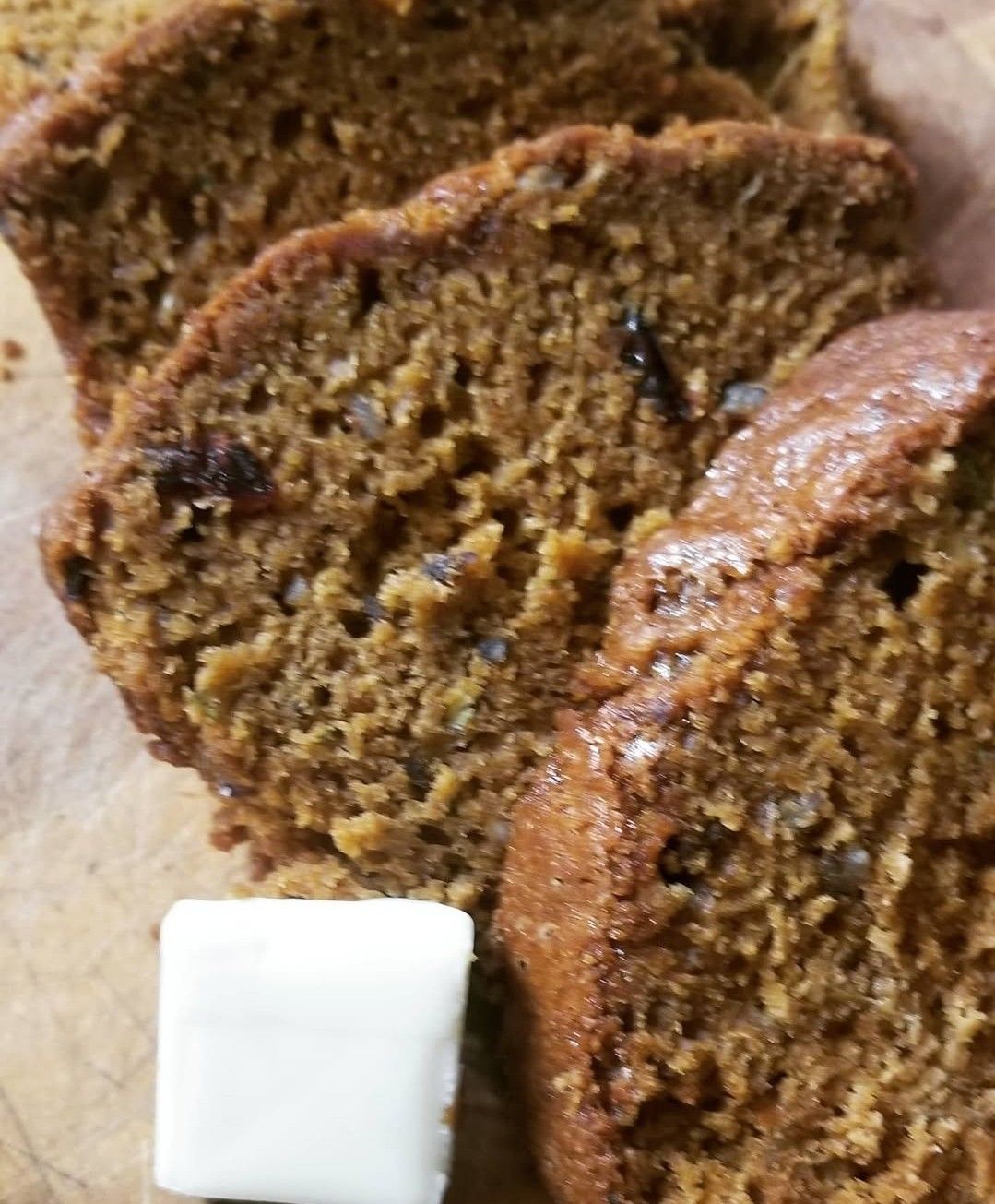 Slices of pumpkin bread with walnuts, served with a square of butter on a wooden surface.
