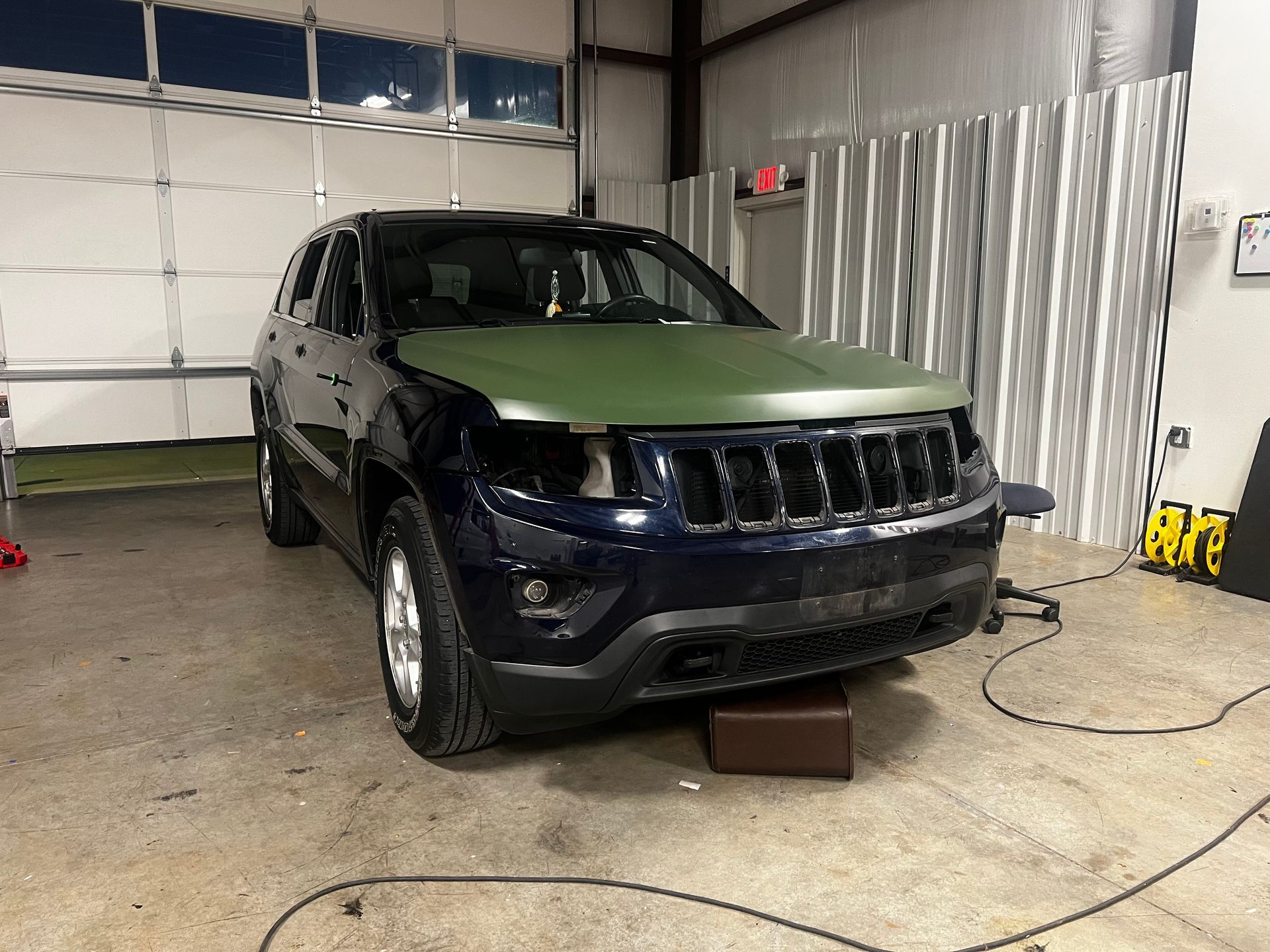 A blue jeep with a green hood is sitting in a garage.