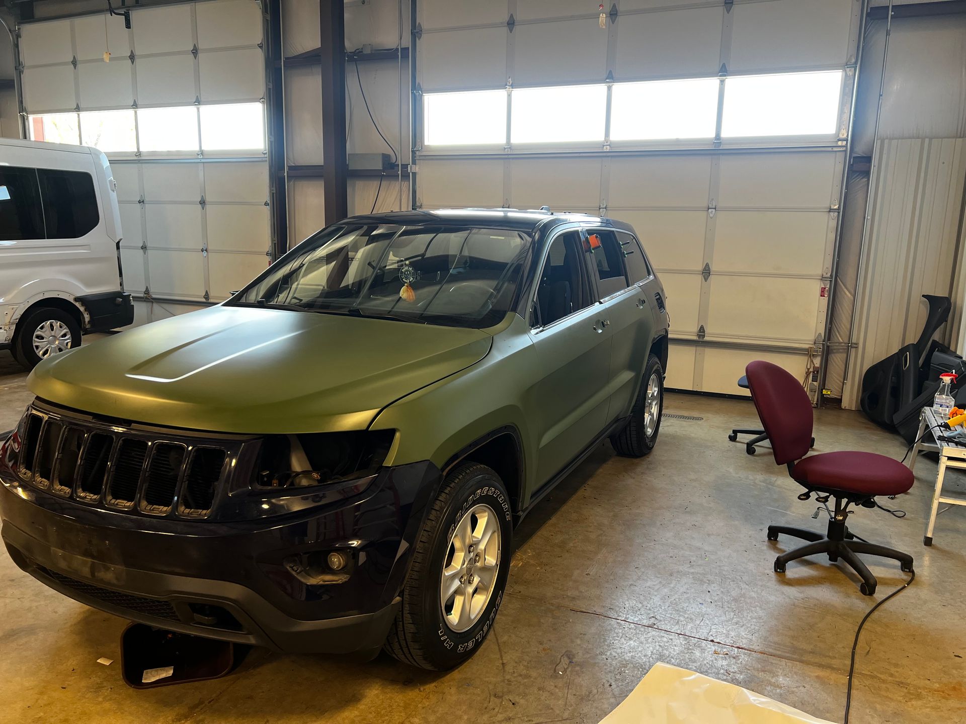 A green jeep is parked in a garage next to a chair.