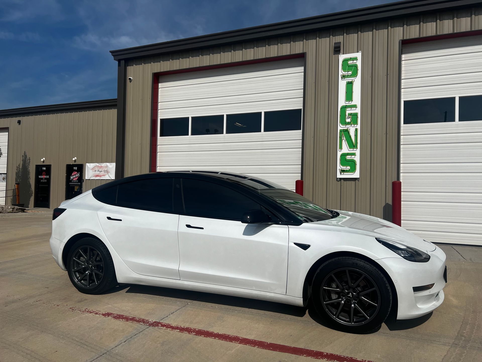 A white tesla model 3 is parked in front of a garage.