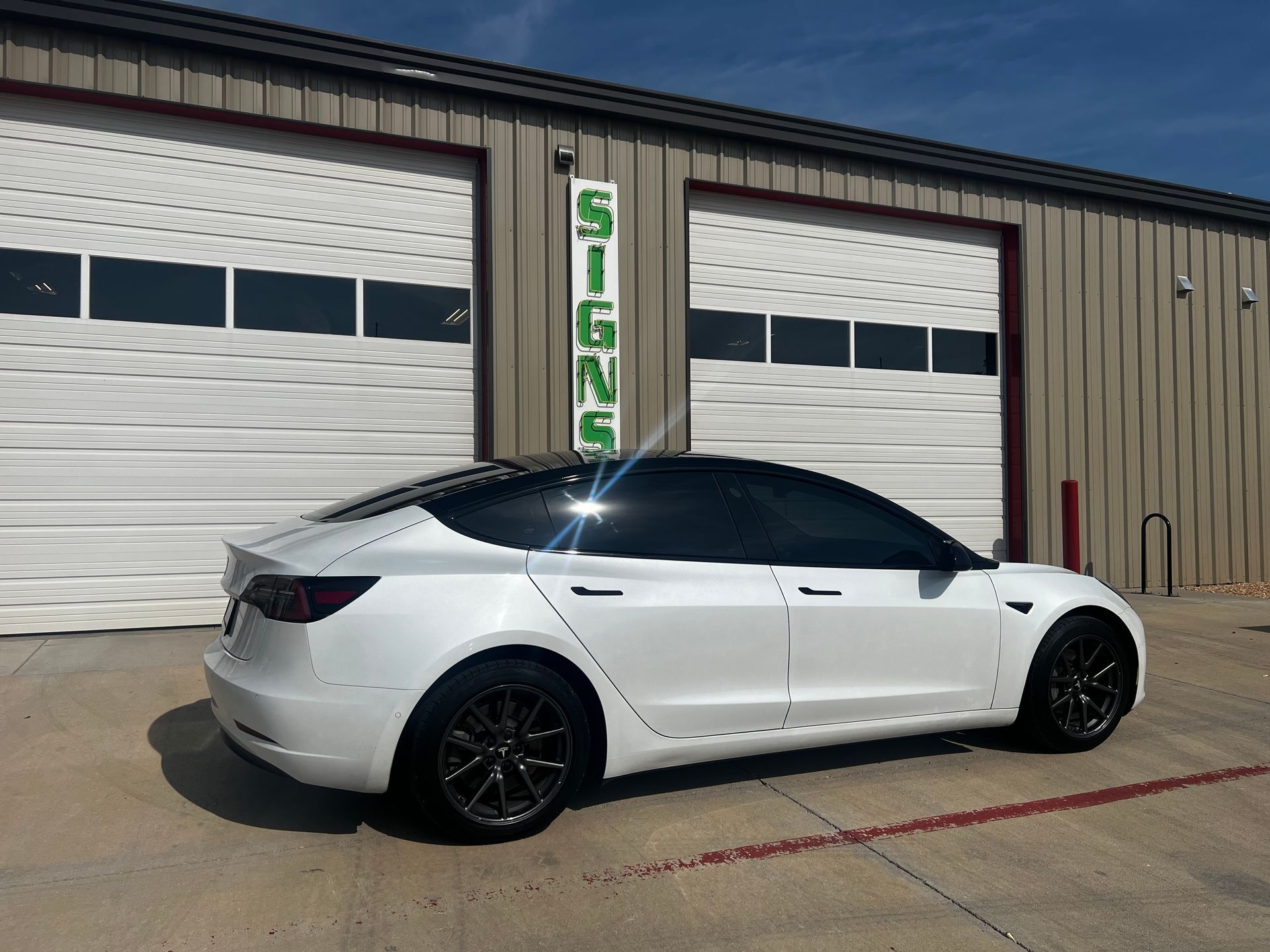 A white tesla model 3 is parked in front of a garage door.