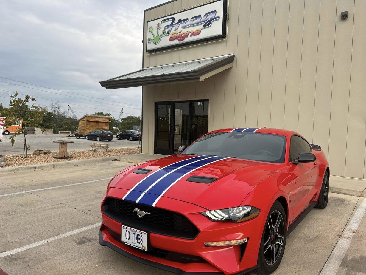 A red ford mustang is parked in front of a car dealership.
