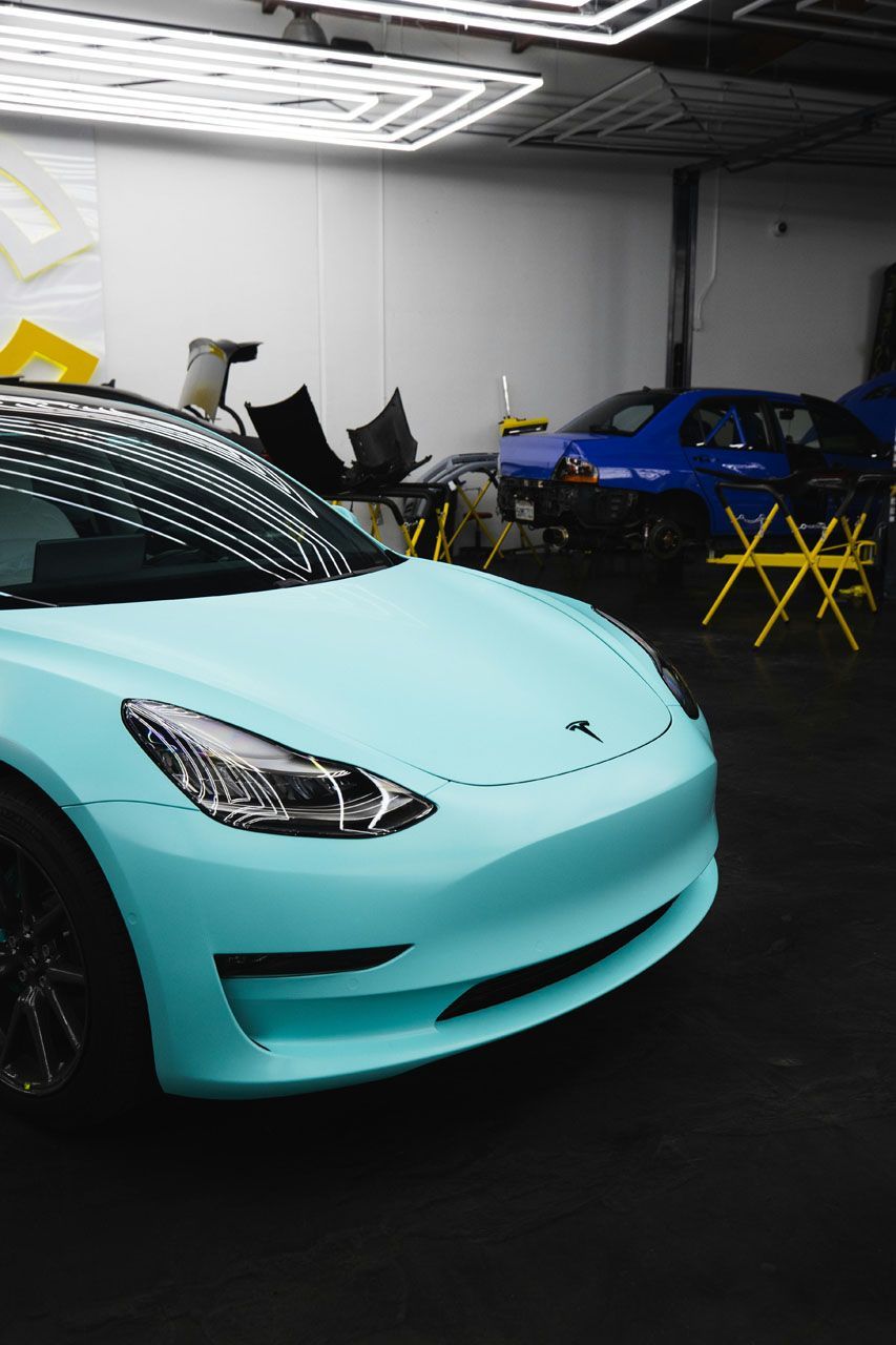 A light blue tesla model 3 is parked in a garage.