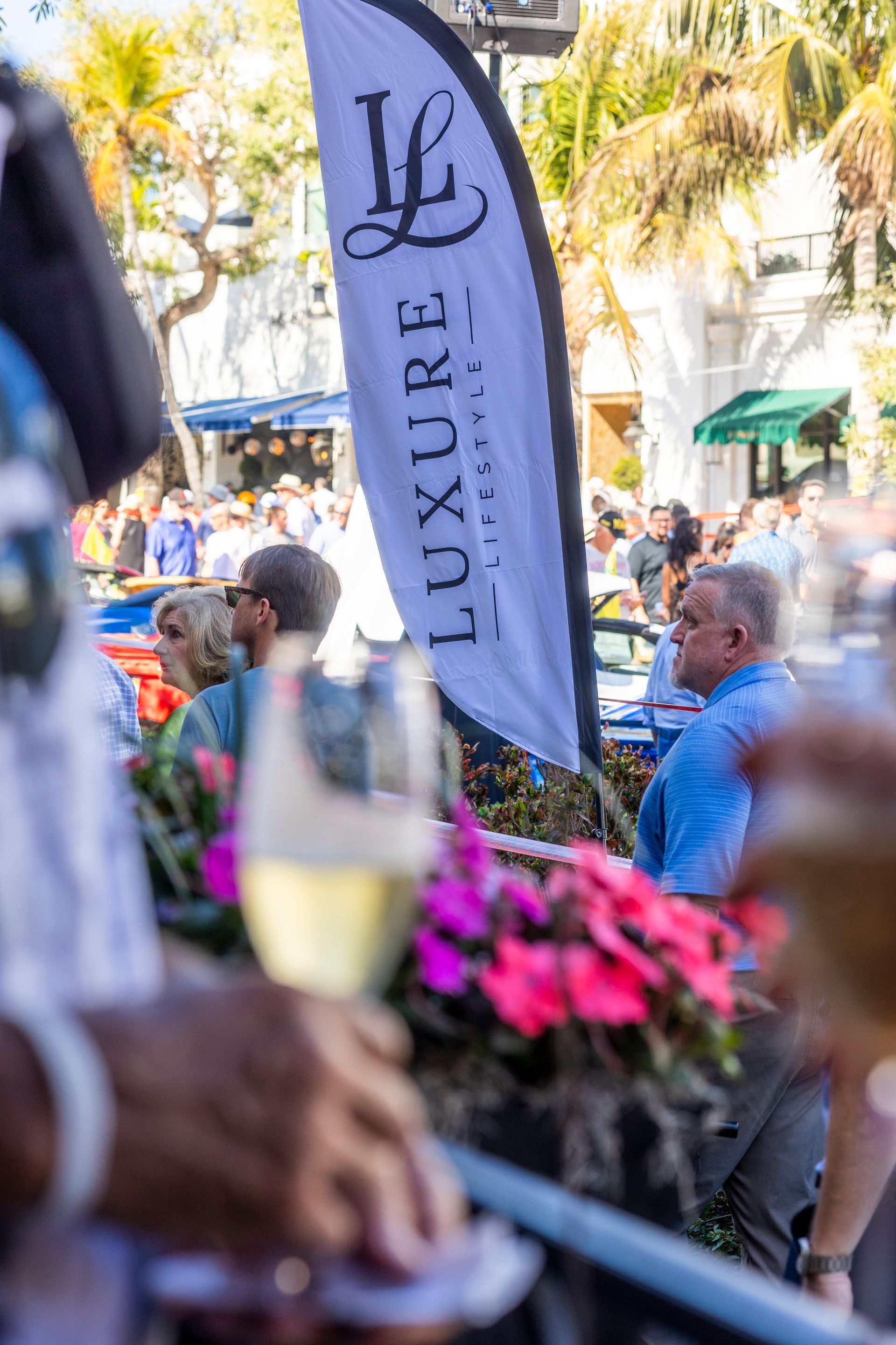 Event with banner: crowd gathered; wine glasses, flowers, and a banner with