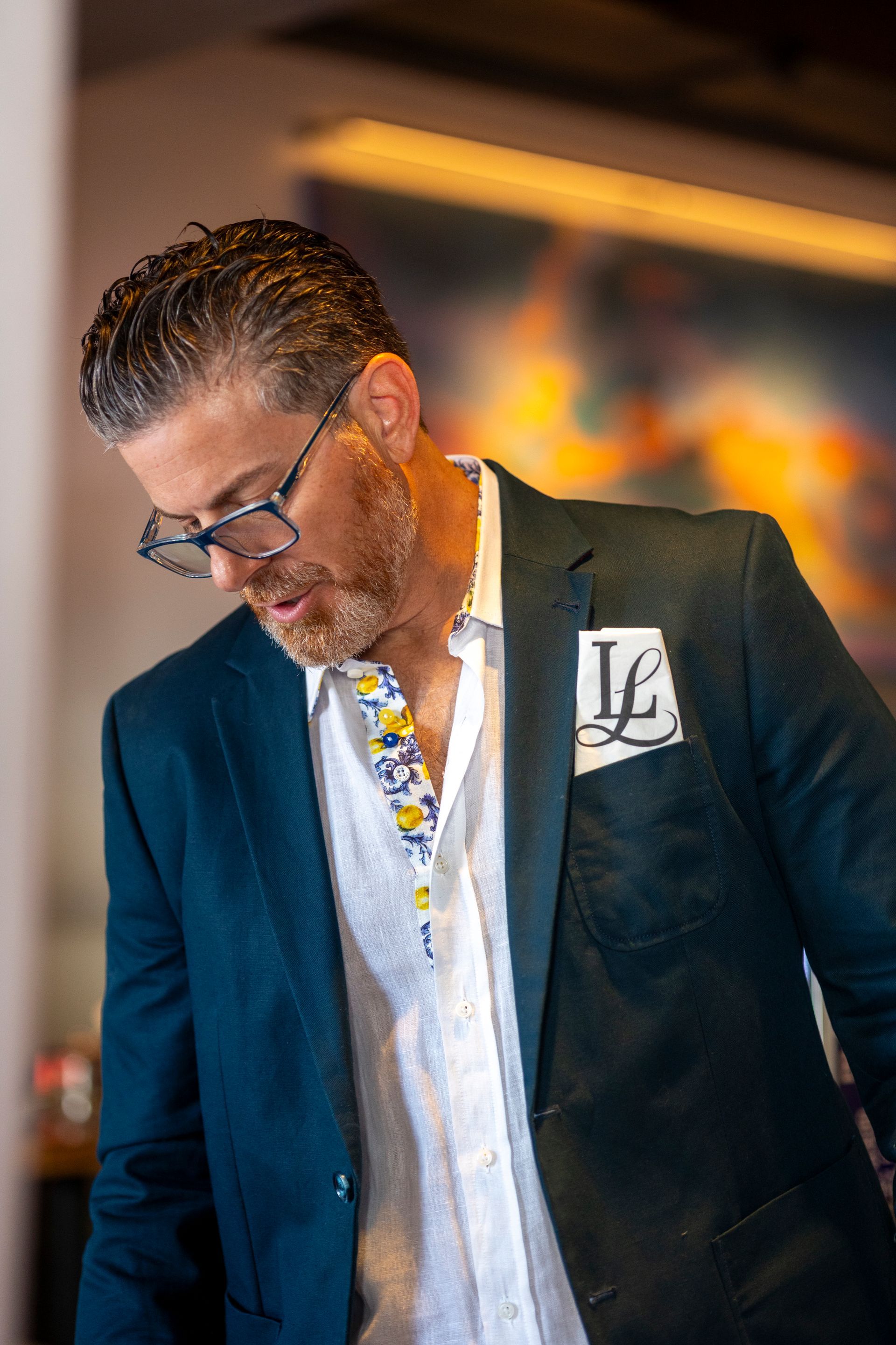 Man in teal blazer and white shirt, looking down, with a floral pocket square.