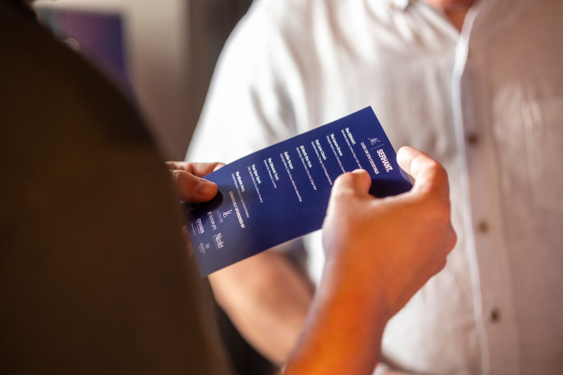 Person holding a blue menu, standing near another person in a white shirt.