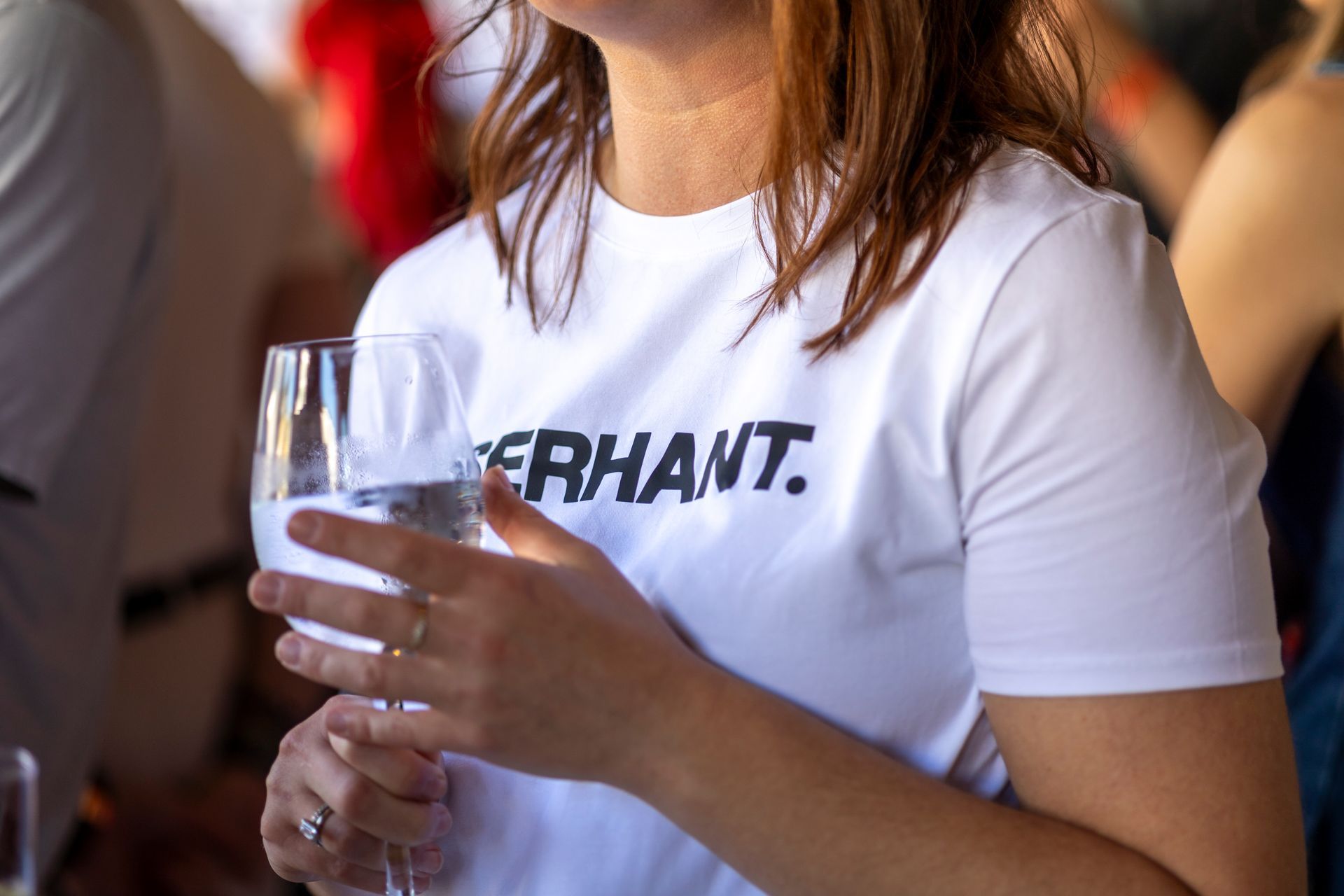 Woman in white t-shirt holding a champagne glass at an outdoor event; the shirt reads