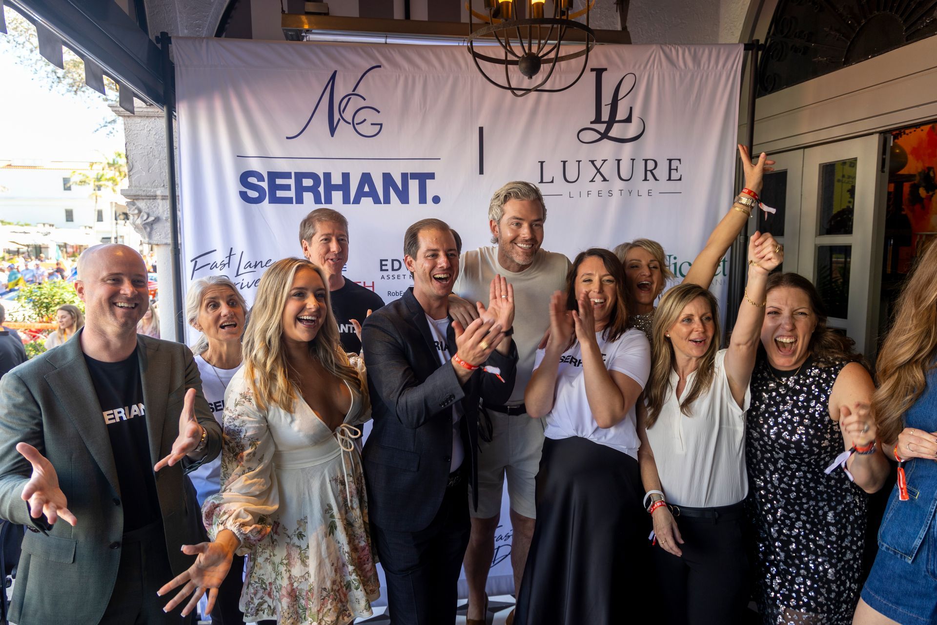 Group of people celebrating in front of a banner with logos. They are clapping, smiling, and excited.