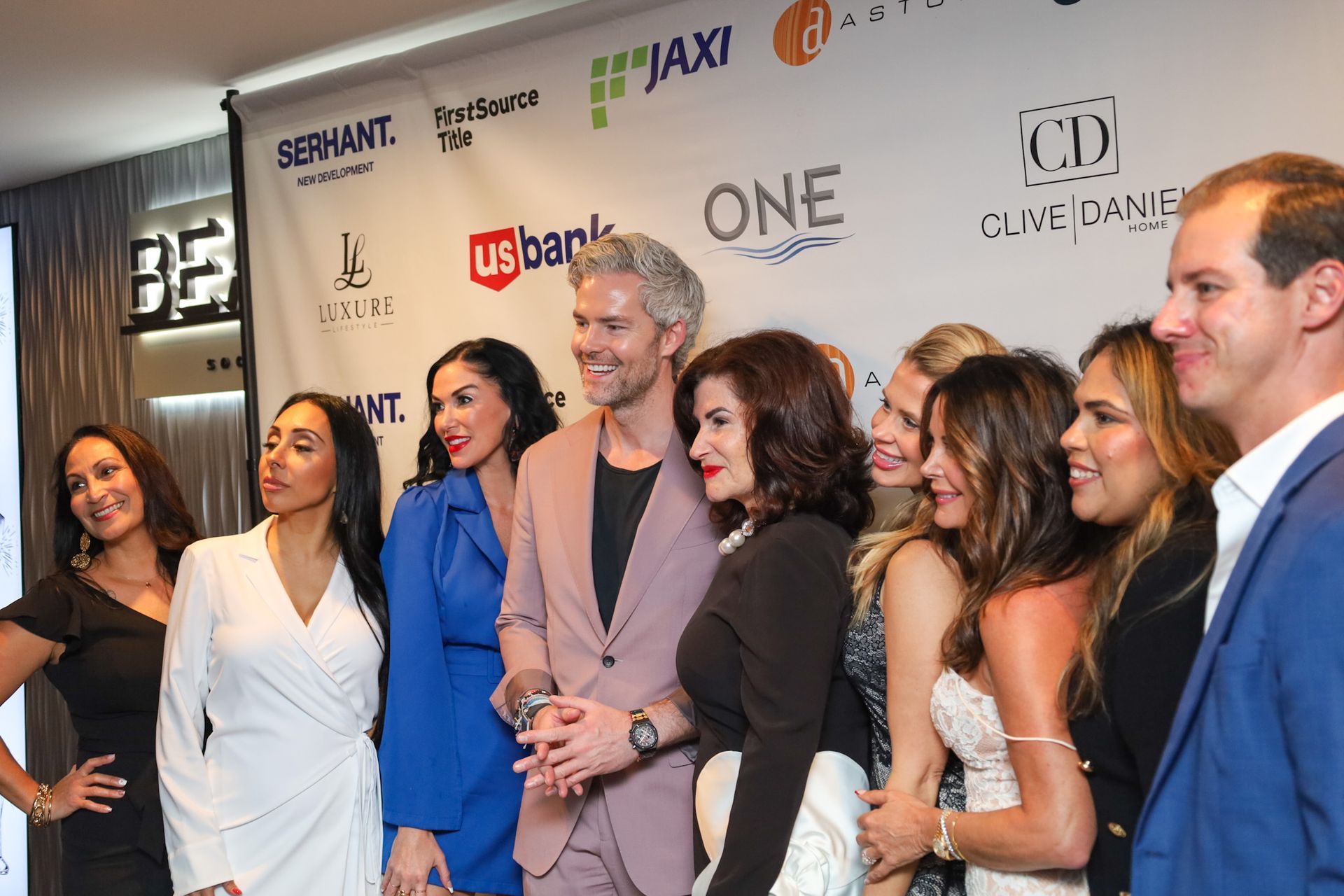 Group of people posing for a photo in front of a backdrop with logos. Some are smiling.