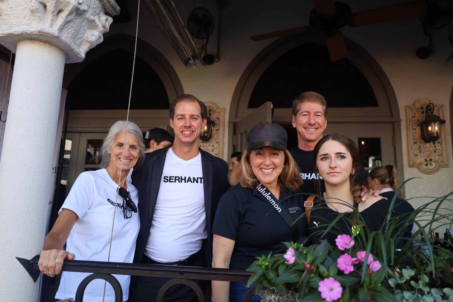Group of five people smiling outside a building, floral planter in the foreground.