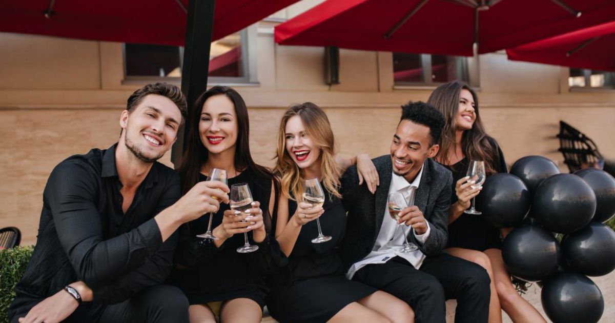 Group of people in black attire toasting with wine glasses outdoors, smiling.