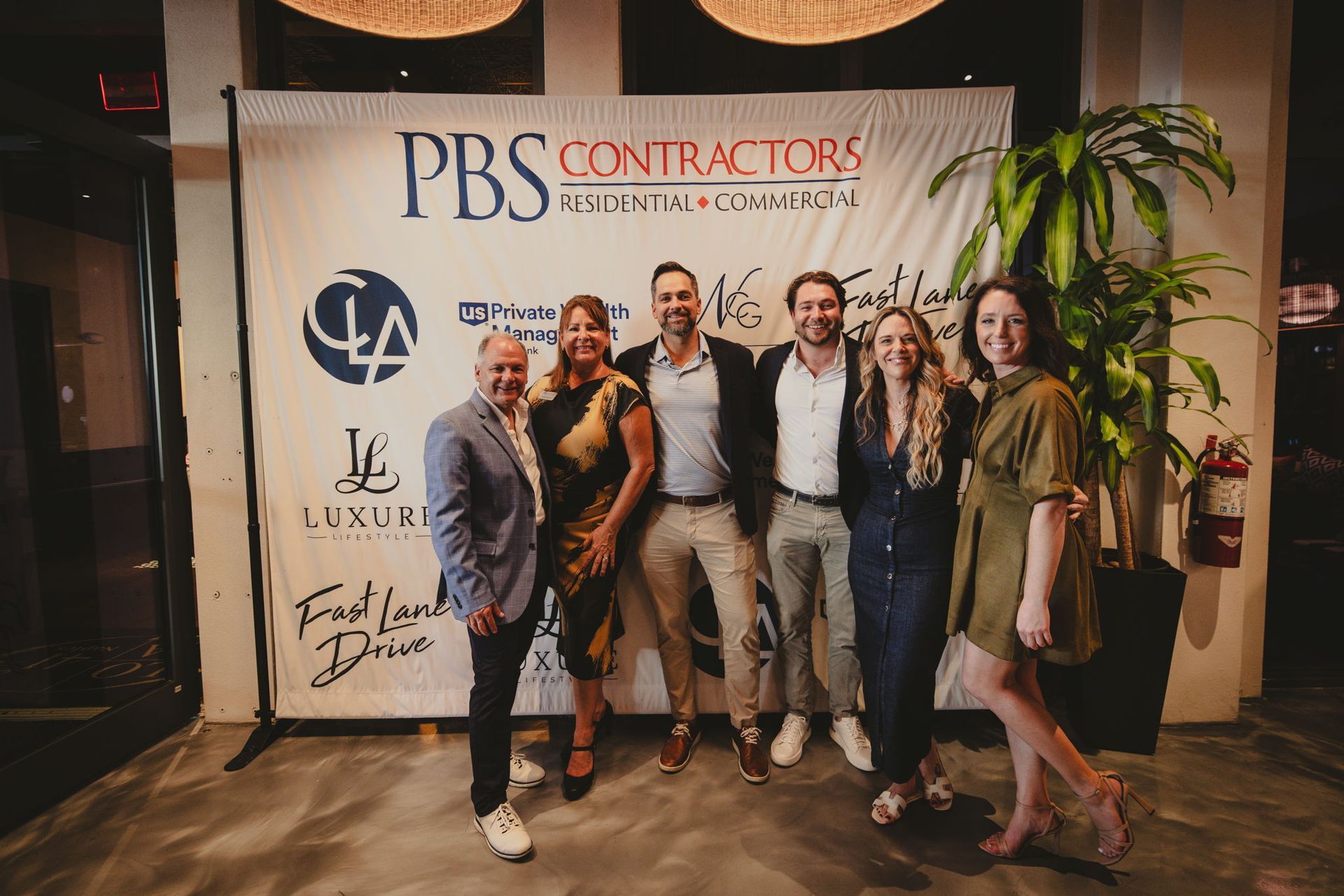 Group of six people posing in front of a PBS Contractors banner at an event.