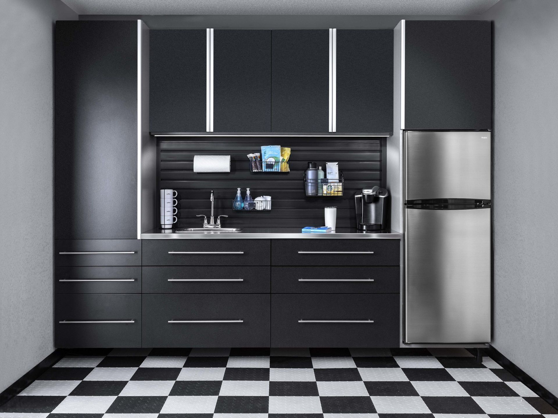 Garage storage space with black cabinets, stainless steel refrigerator, sink, and checkered Swisstrax flooring.