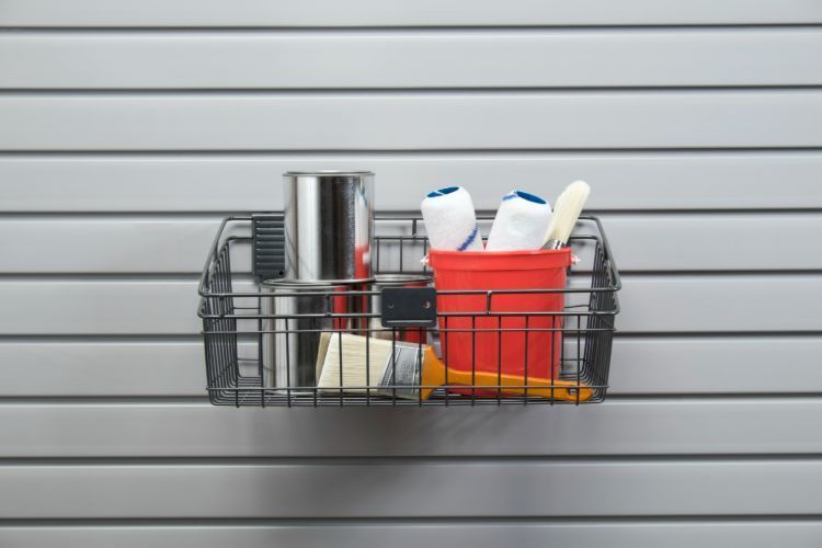 Black wire basket holding paint supplies on a slatted gray wall.