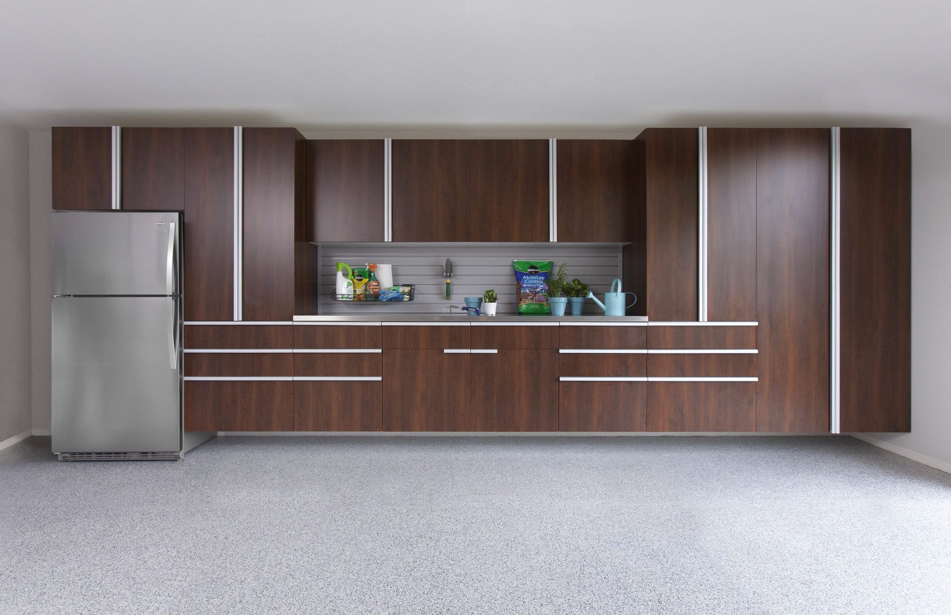 A sleek, dark wood garage cabinet system with integrated shelving and a stainless steel refrigerator against a wall.