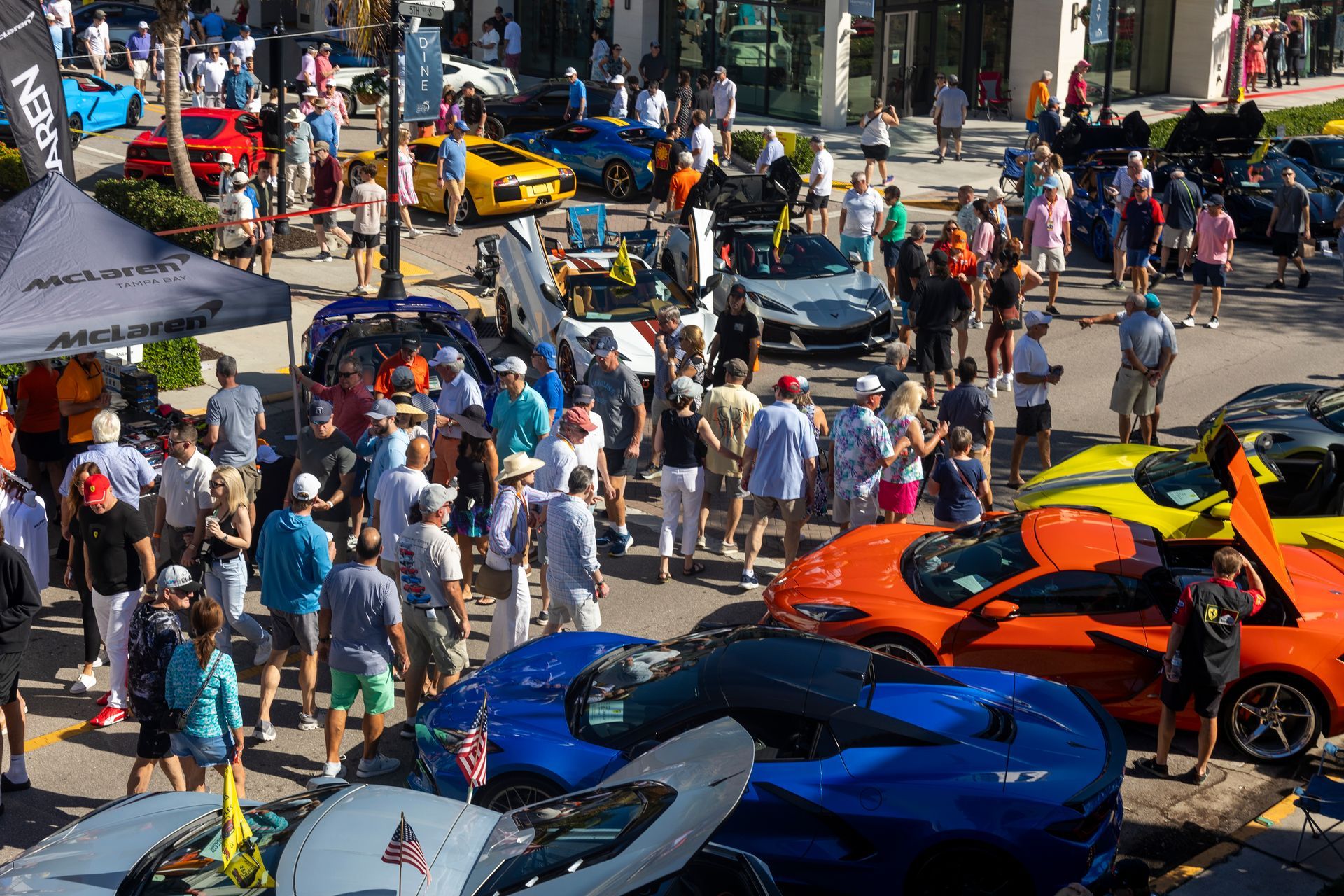 Car show with crowd: Colorful sports cars on display; people milling around them outdoors.