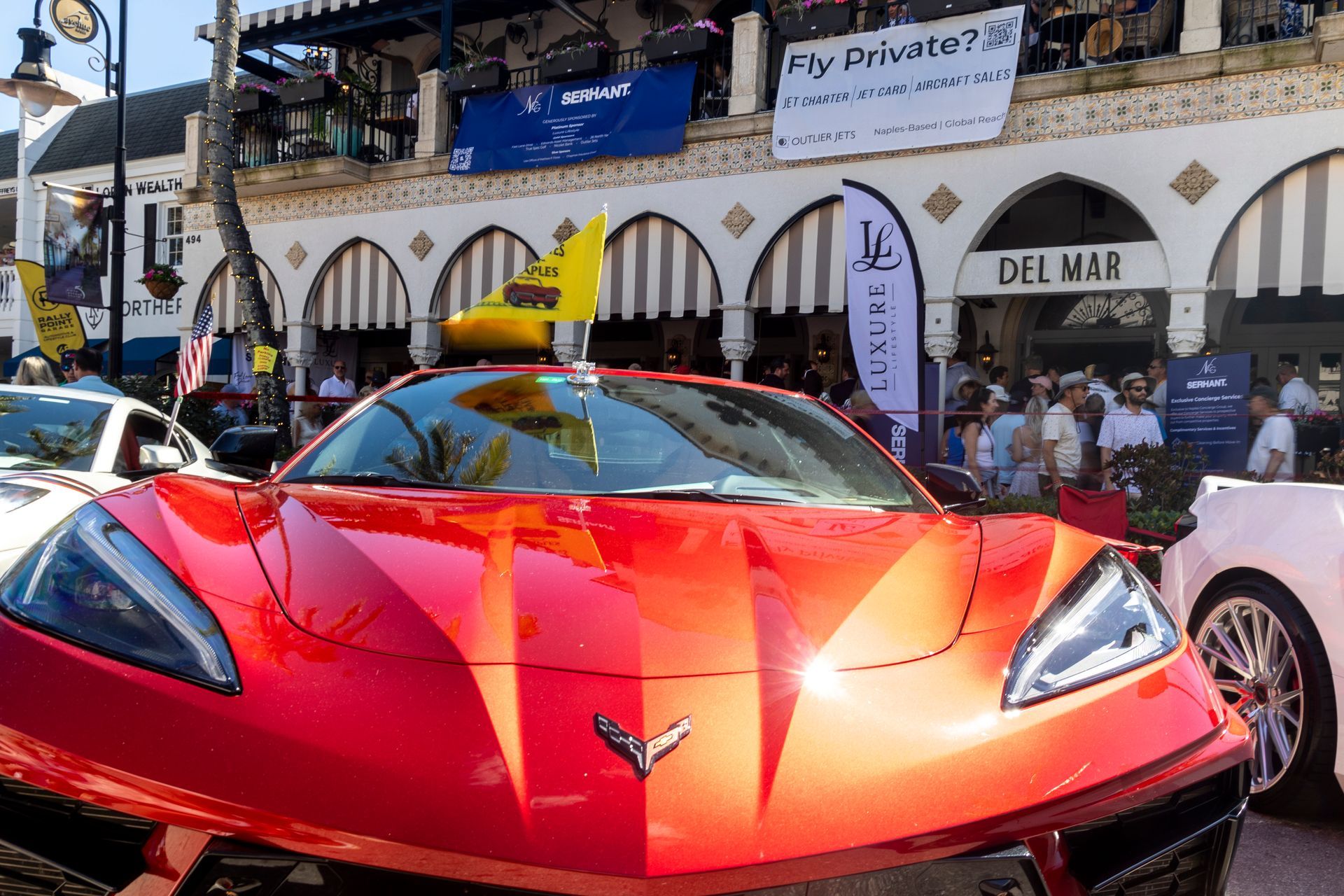 Red sports car parked on a street with Del Mar sign and people in the background.