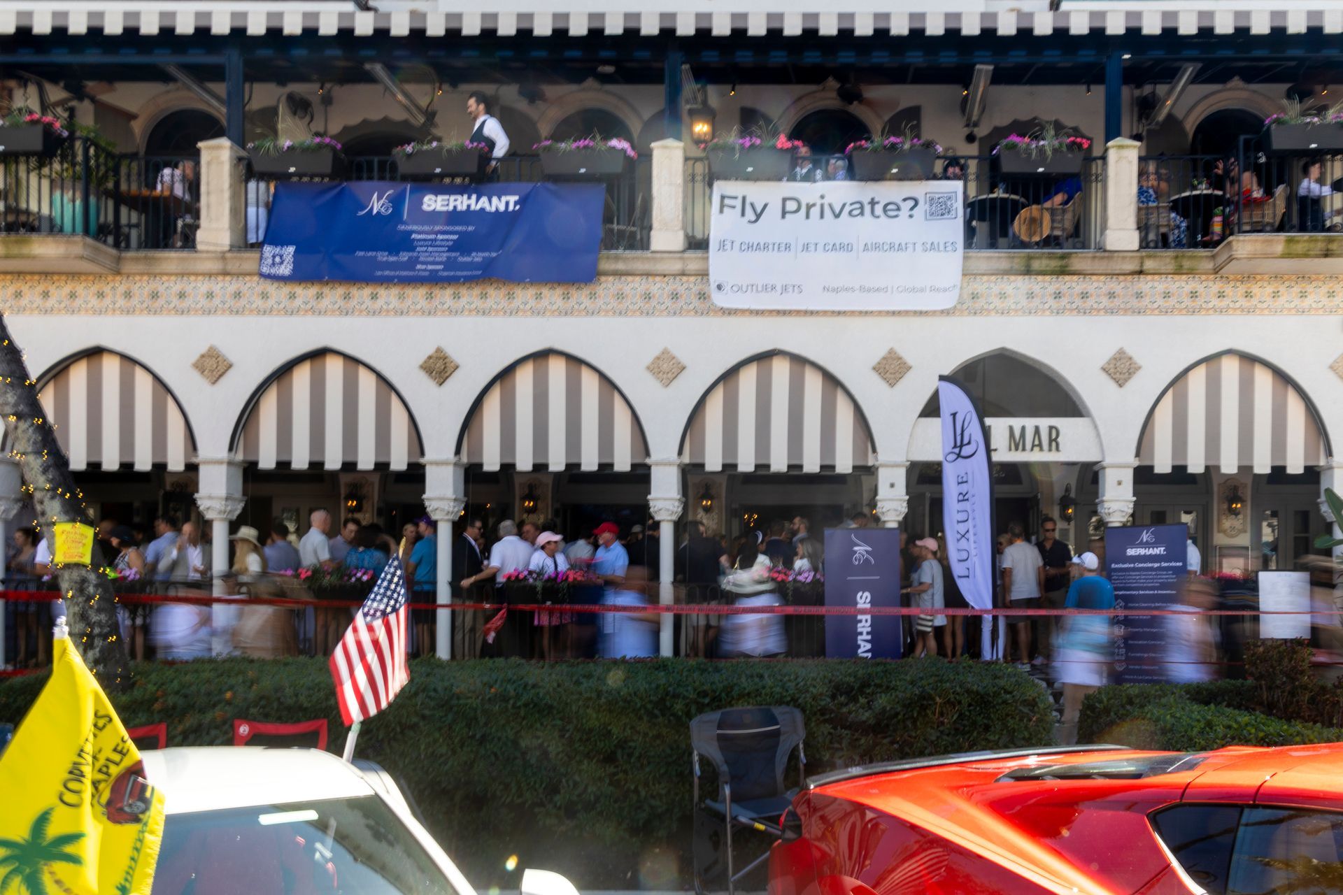 Exterior of a building with people gathered. Banners for a company and