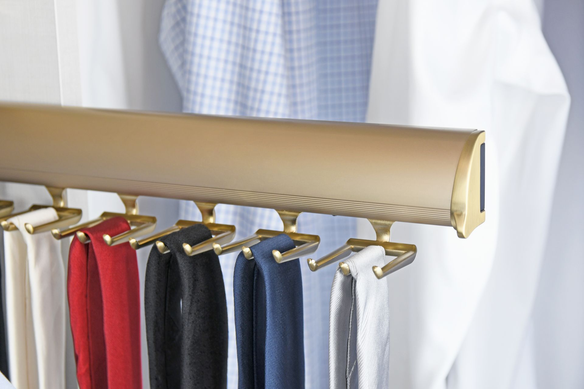 Gold tie rack with several colorful ties hanging in a closet.