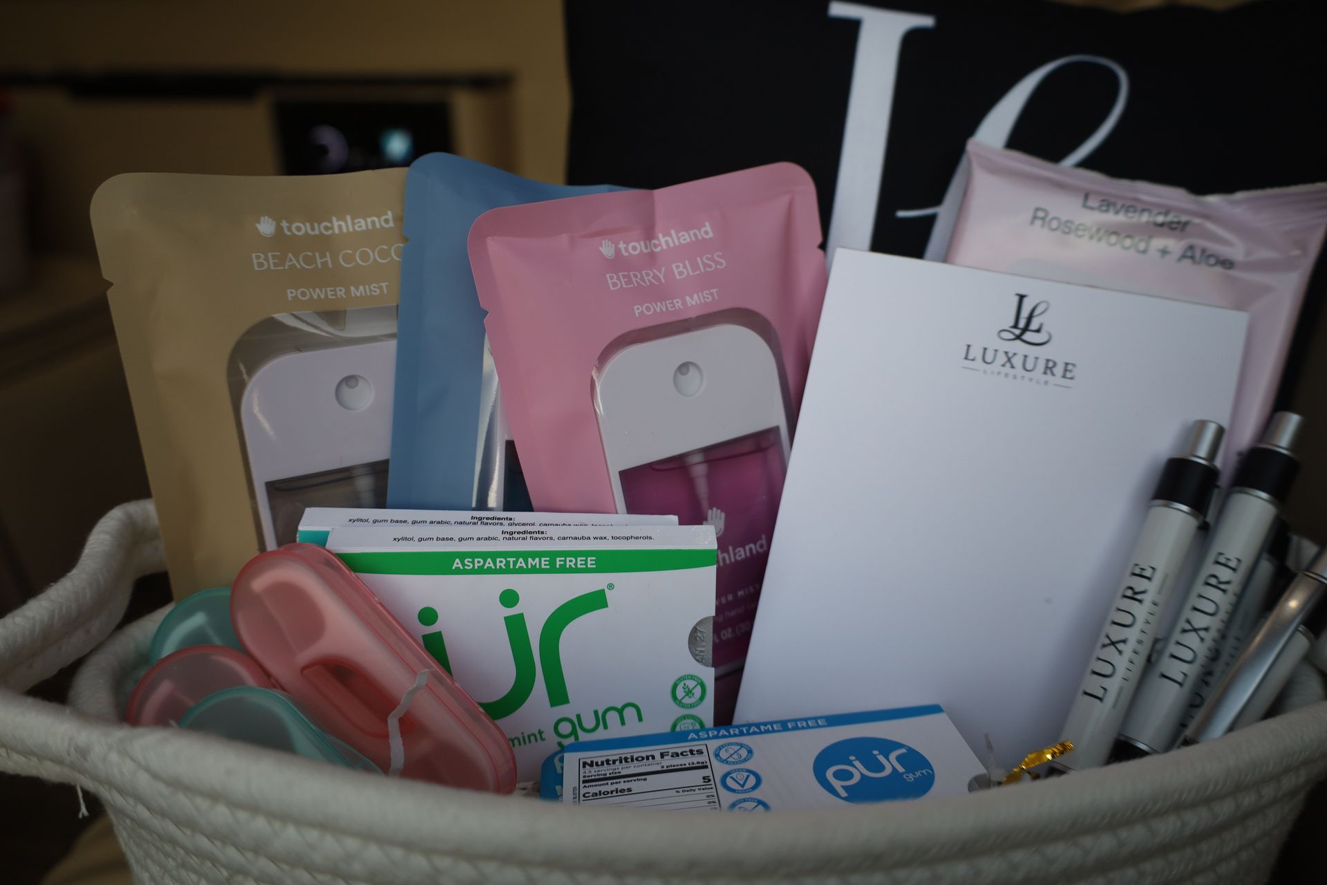 Basket of self-care items: spray bottles, notepad, pens, gum, face masks.