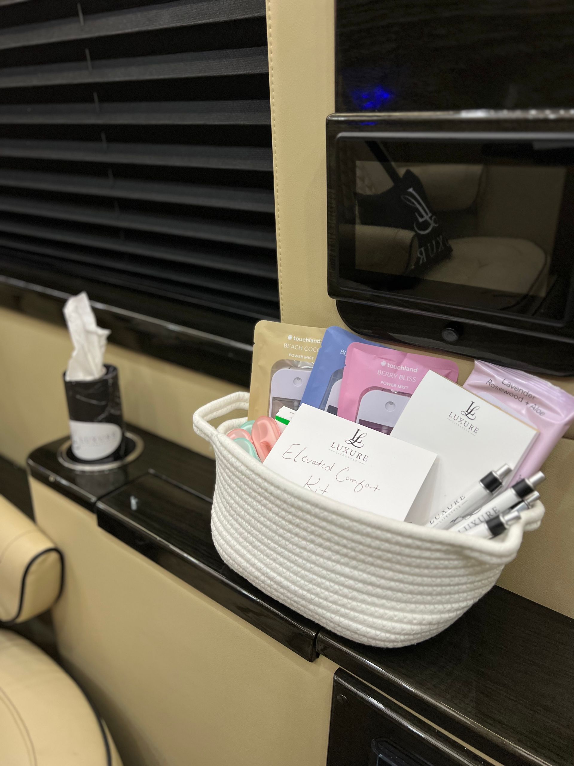White rope basket with assorted items sits on a dark shelf next to a tissue holder and small screen.